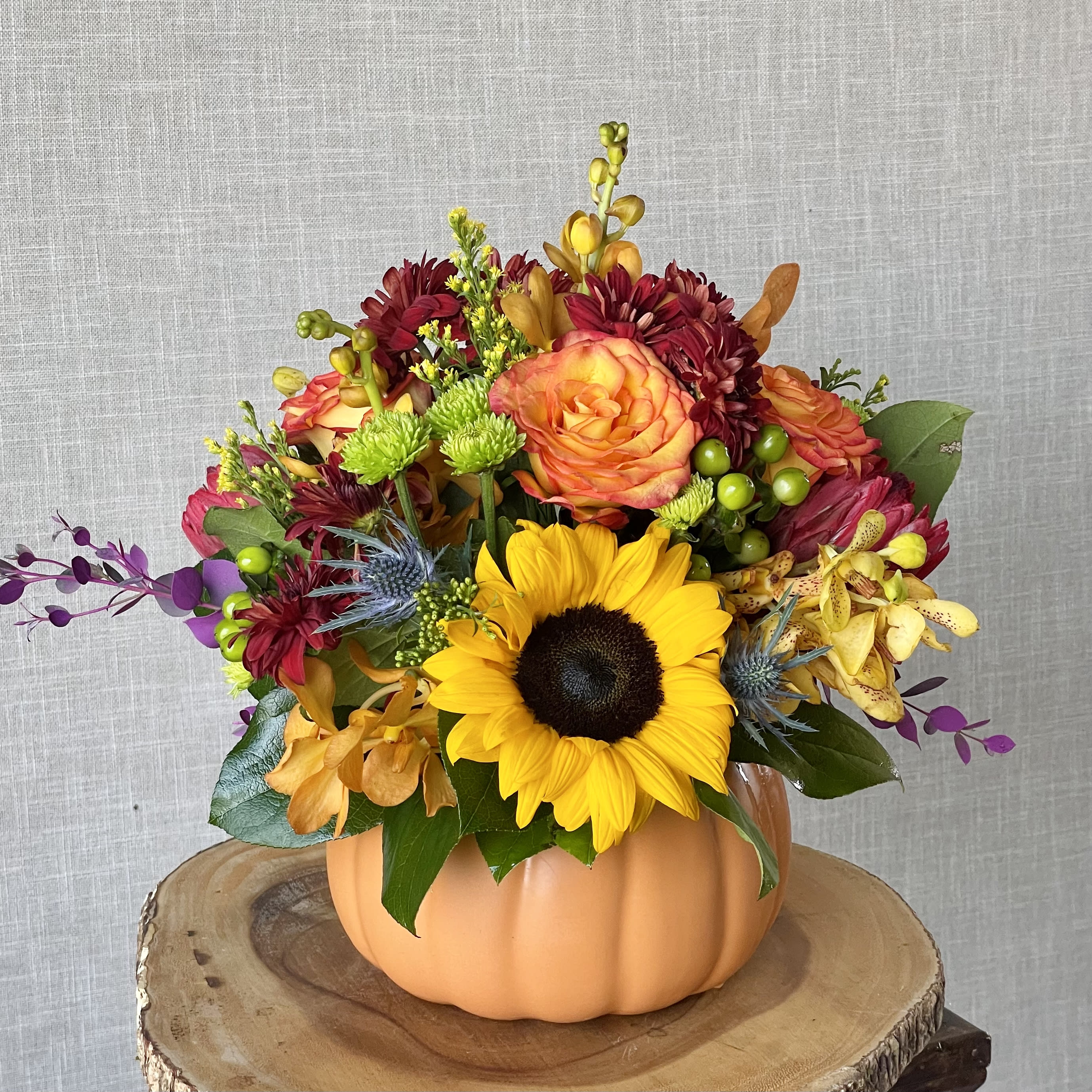 Mixed bouquet in a pumpkin-shaped vase with a sunflower and orange roses