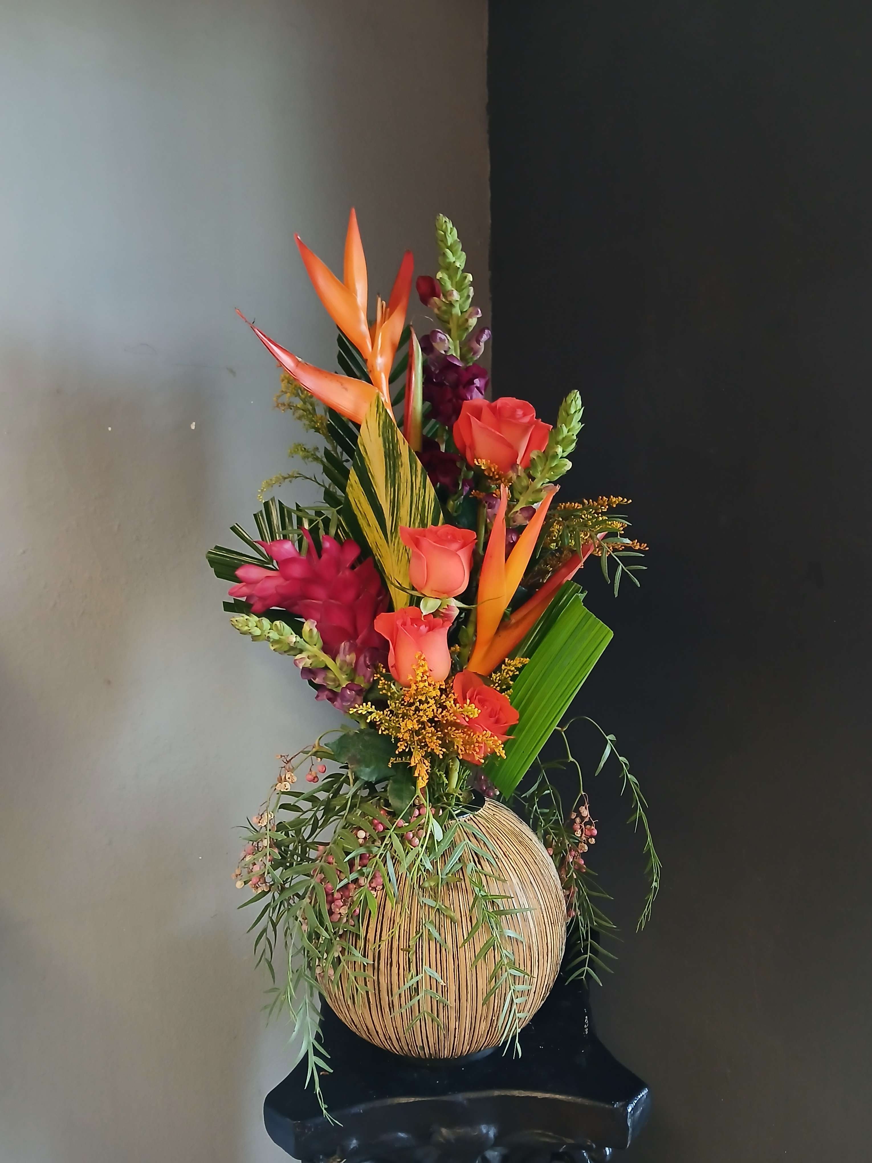 Tropical bouquet with orange birds of paradise and coral roses in a woven vase