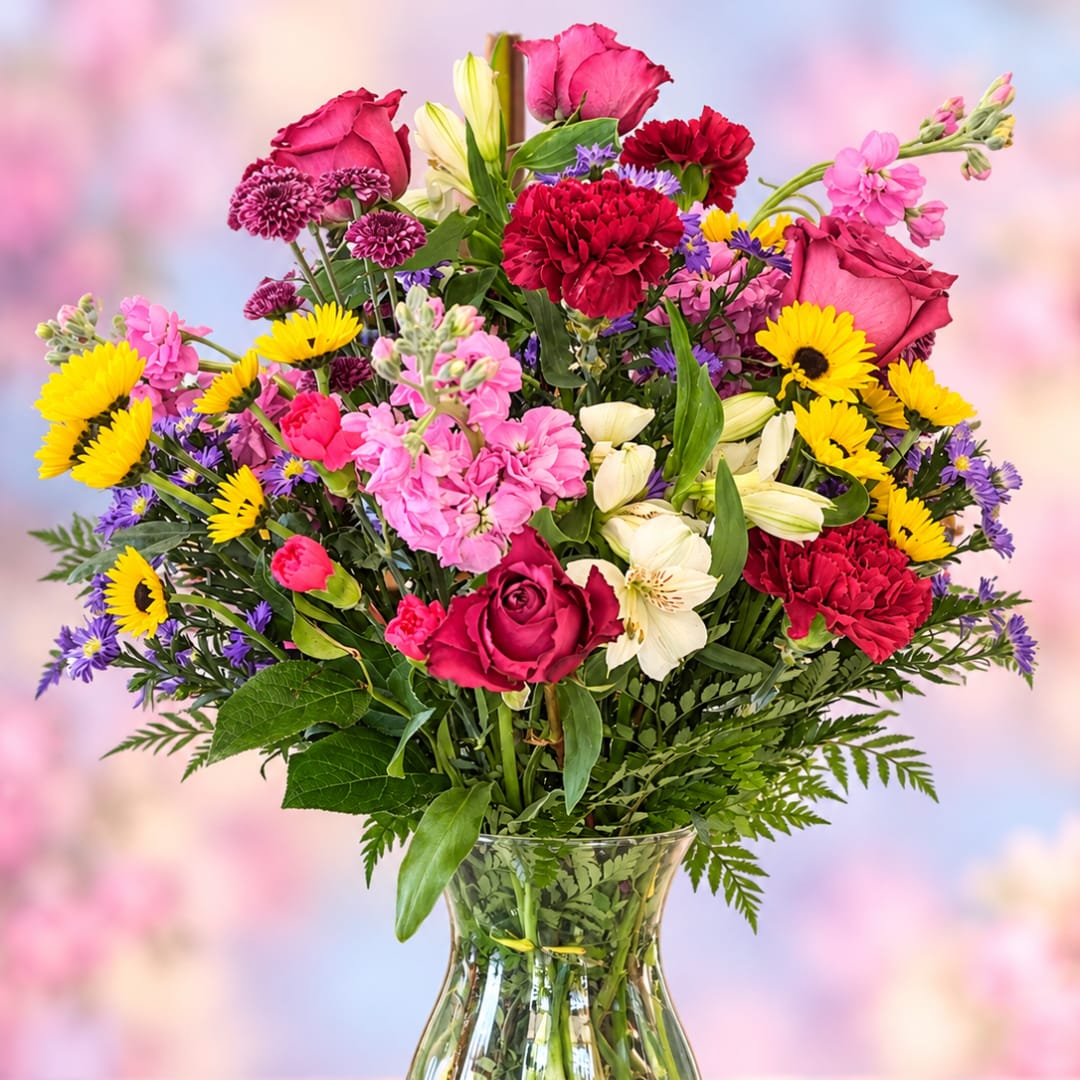 Mixed bouquet of pink, red, yellow, and white flowers in a clear glass vase