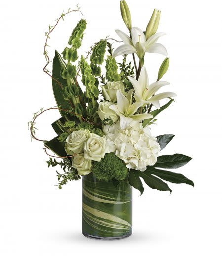 Tall white lilies, roses, and hydrangeas with green accents in a leaf-lined glass cylinder vase