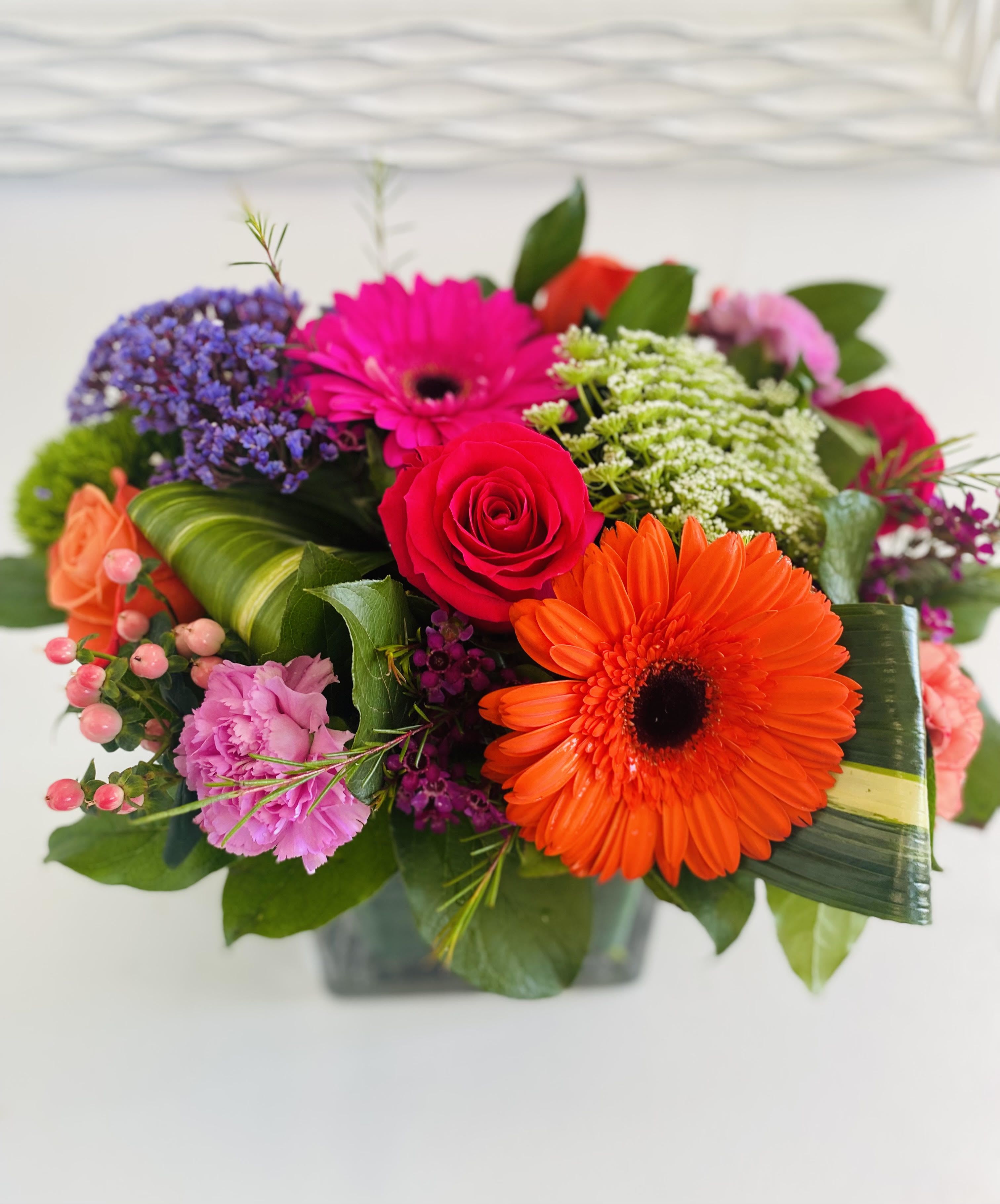 Bright mixed bouquet of orange gerbera daisies, hot pink roses and other blooms in a low glass cube vase