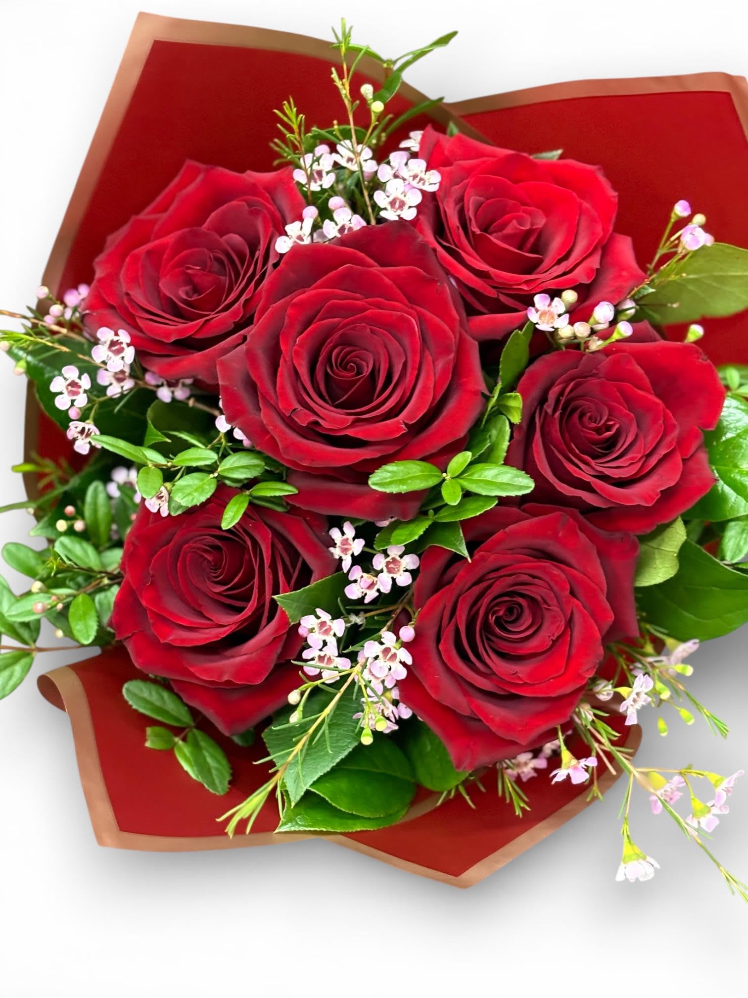 Hand-tied bouquet of red roses with tiny pink filler flowers wrapped in red paper.