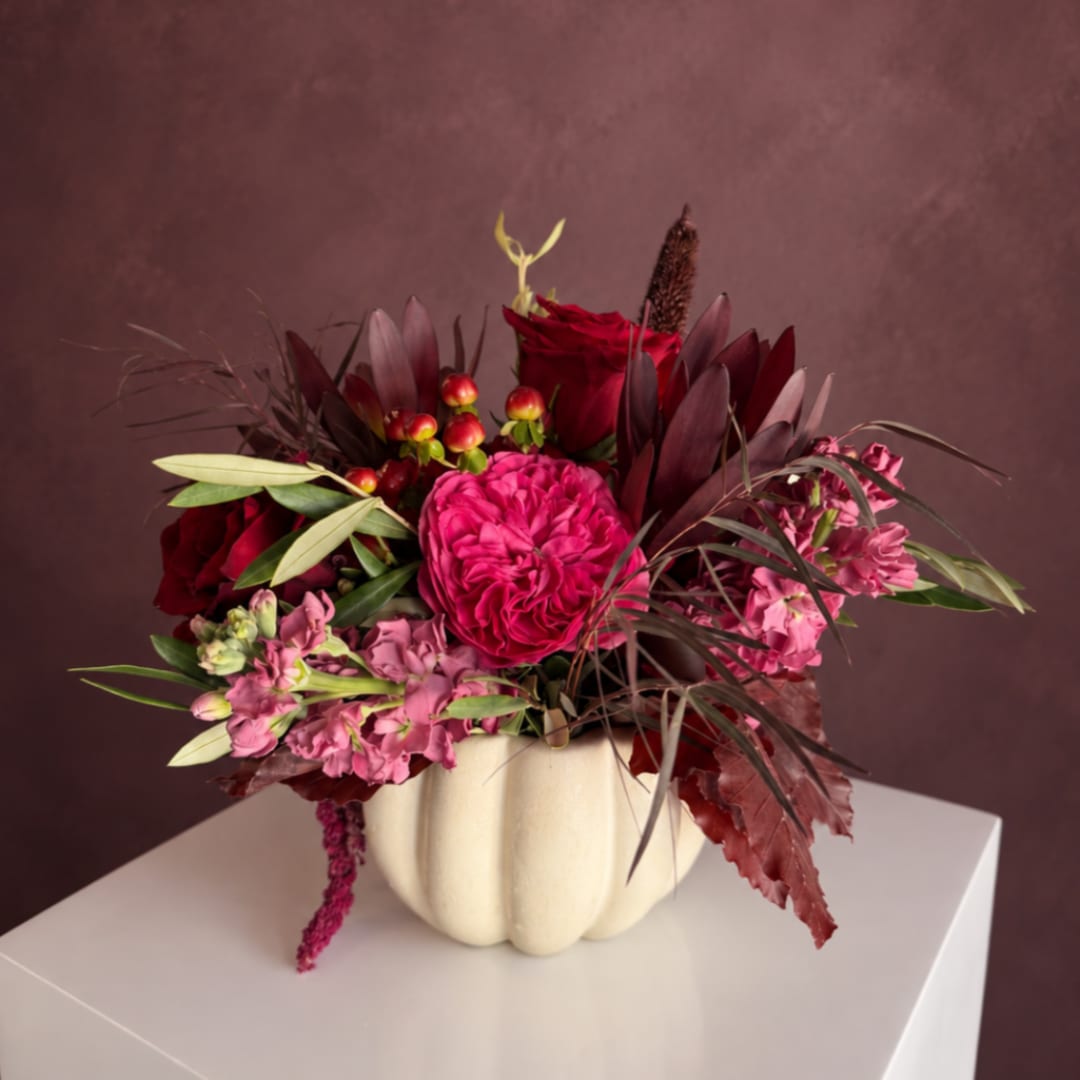 Red and pink floral arrangement in a cream pumpkin vase