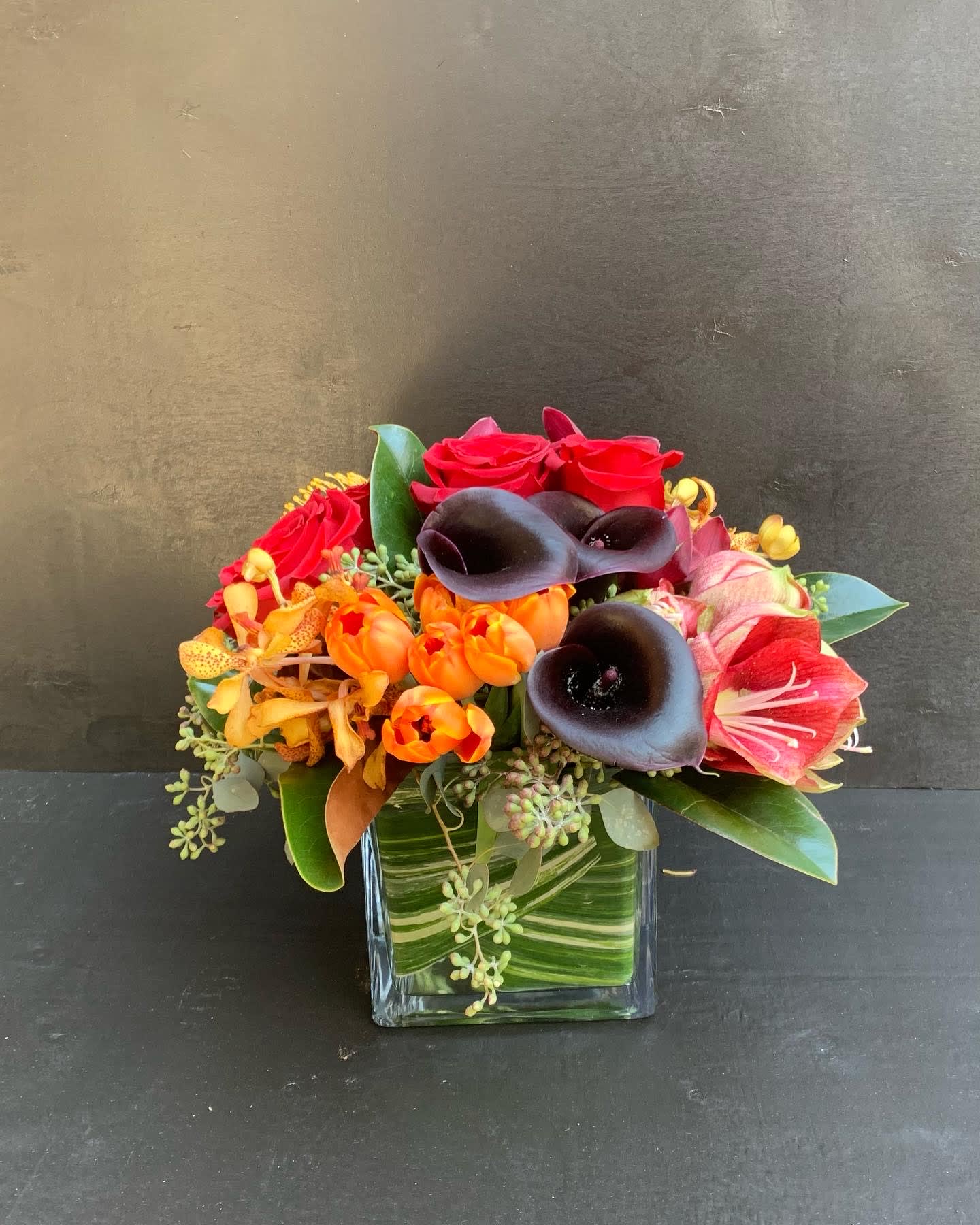 Mixed bouquet with red roses, black calla lilies, and orange tulips in a glass vase