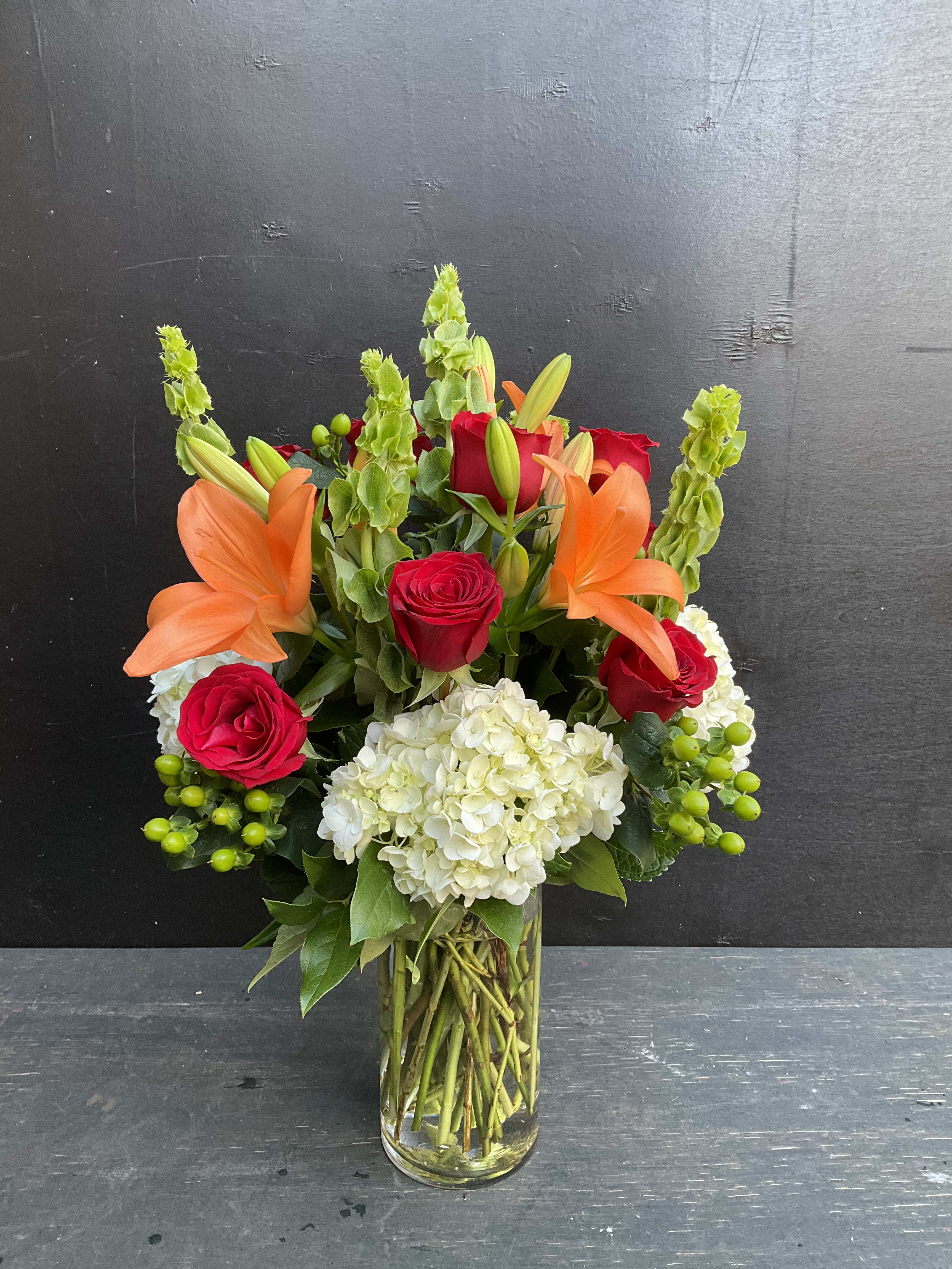 Bouquet of red roses, orange lilies, and white hydrangea in a glass vase