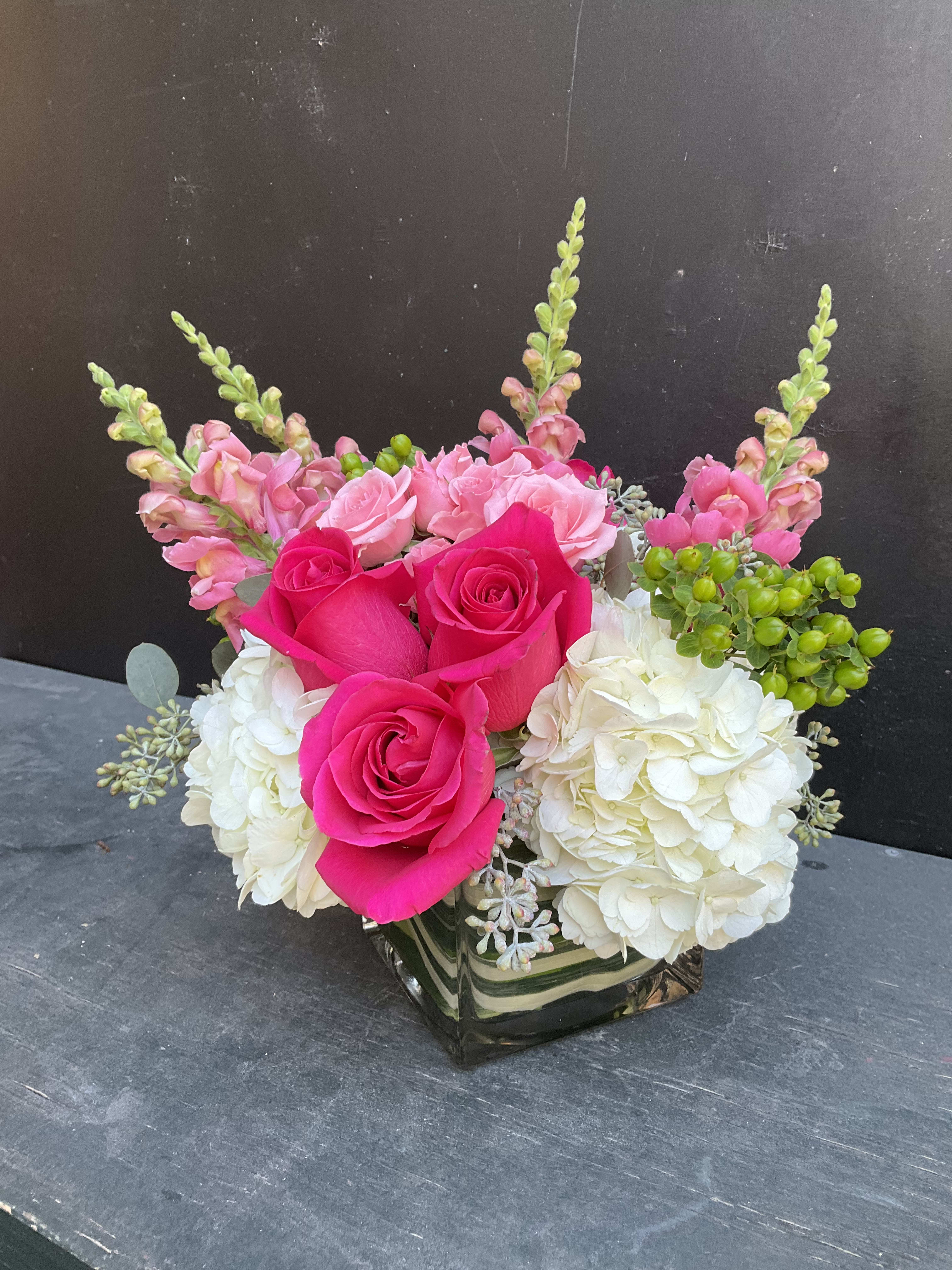 Pink roses and white hydrangeas arranged in a square glass vase