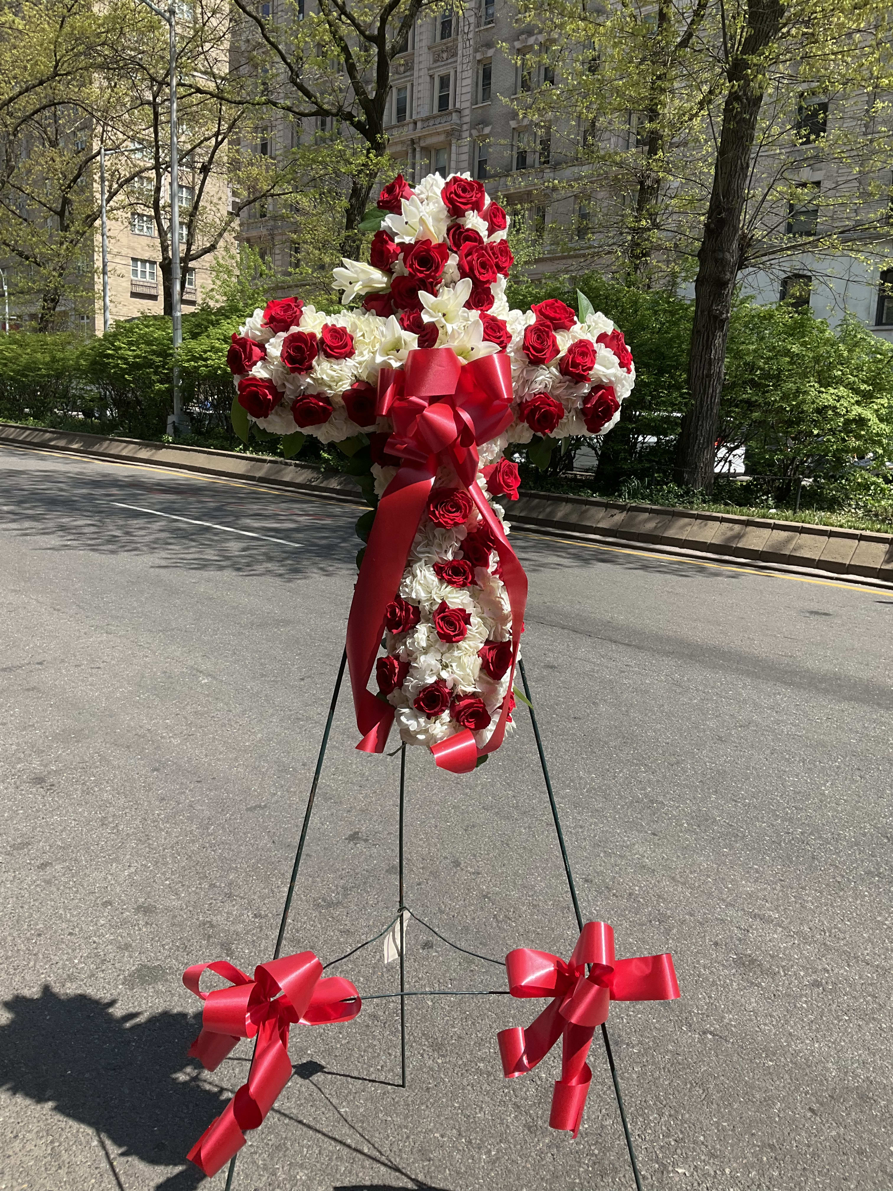 Standing floral cross of red roses and white flowers with red ribbon