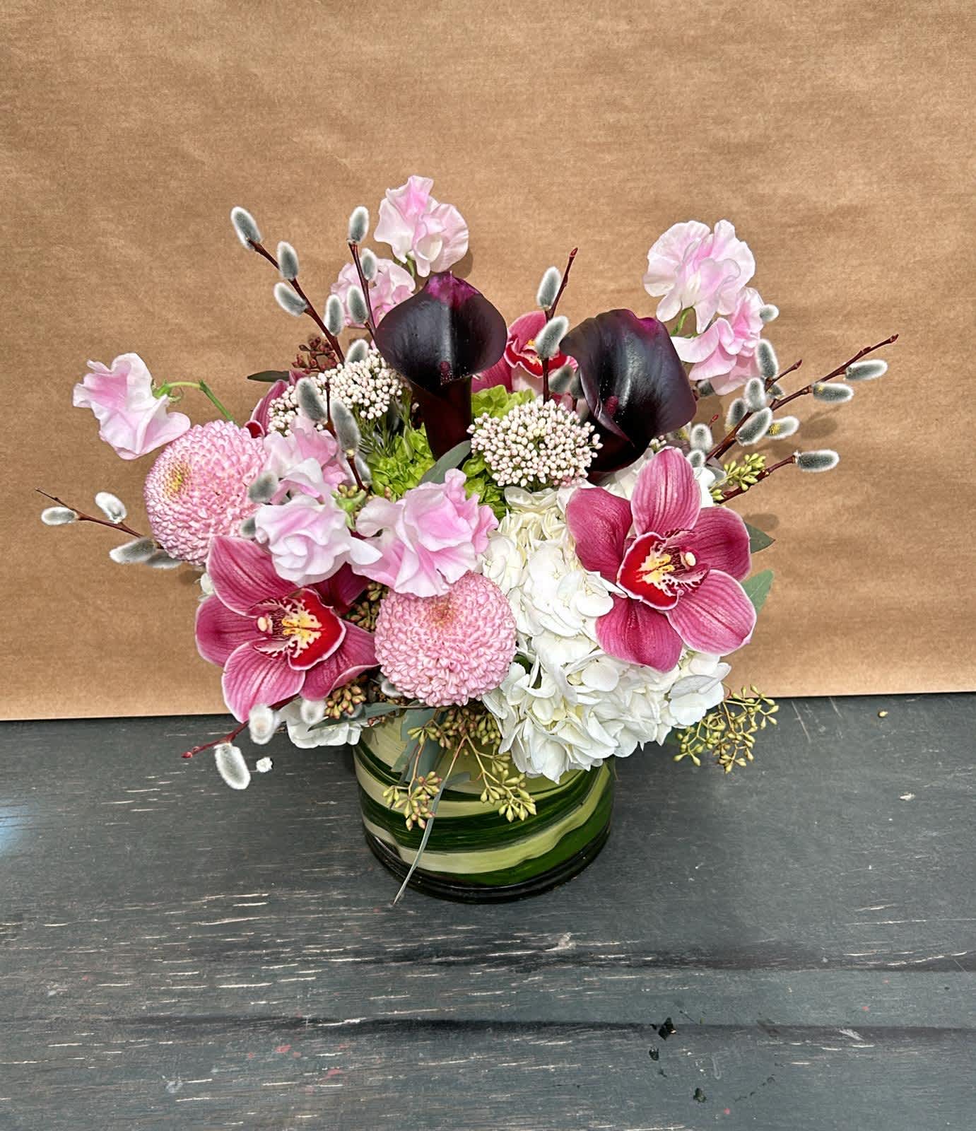 Pink and white floral arrangement with dark calla lilies in a green glass vase