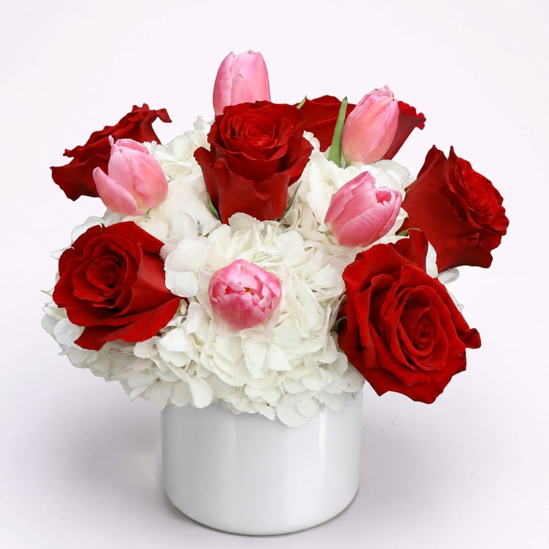 Red roses and pink tulips in a white vase with white hydrangeas