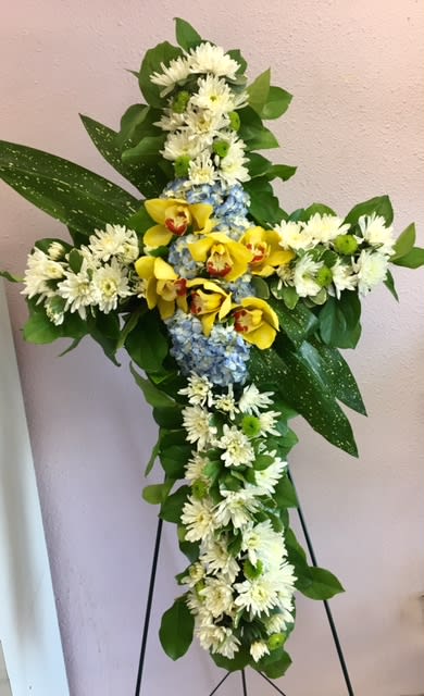 Cross-shaped floral arrangement with yellow orchids, white daisies, and blue hydrangea