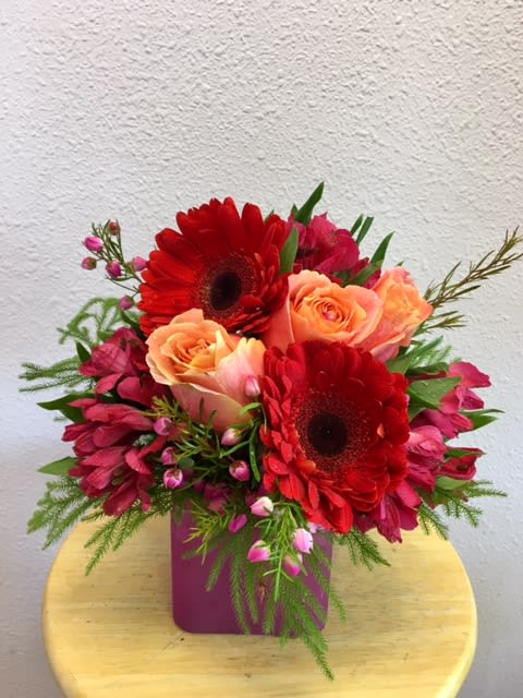 Lovely Flames by Forever Flowers - A compact arrangement with warm colored blooms. Contains red gerberas, peach roses, red alstroemerias, and greens. 