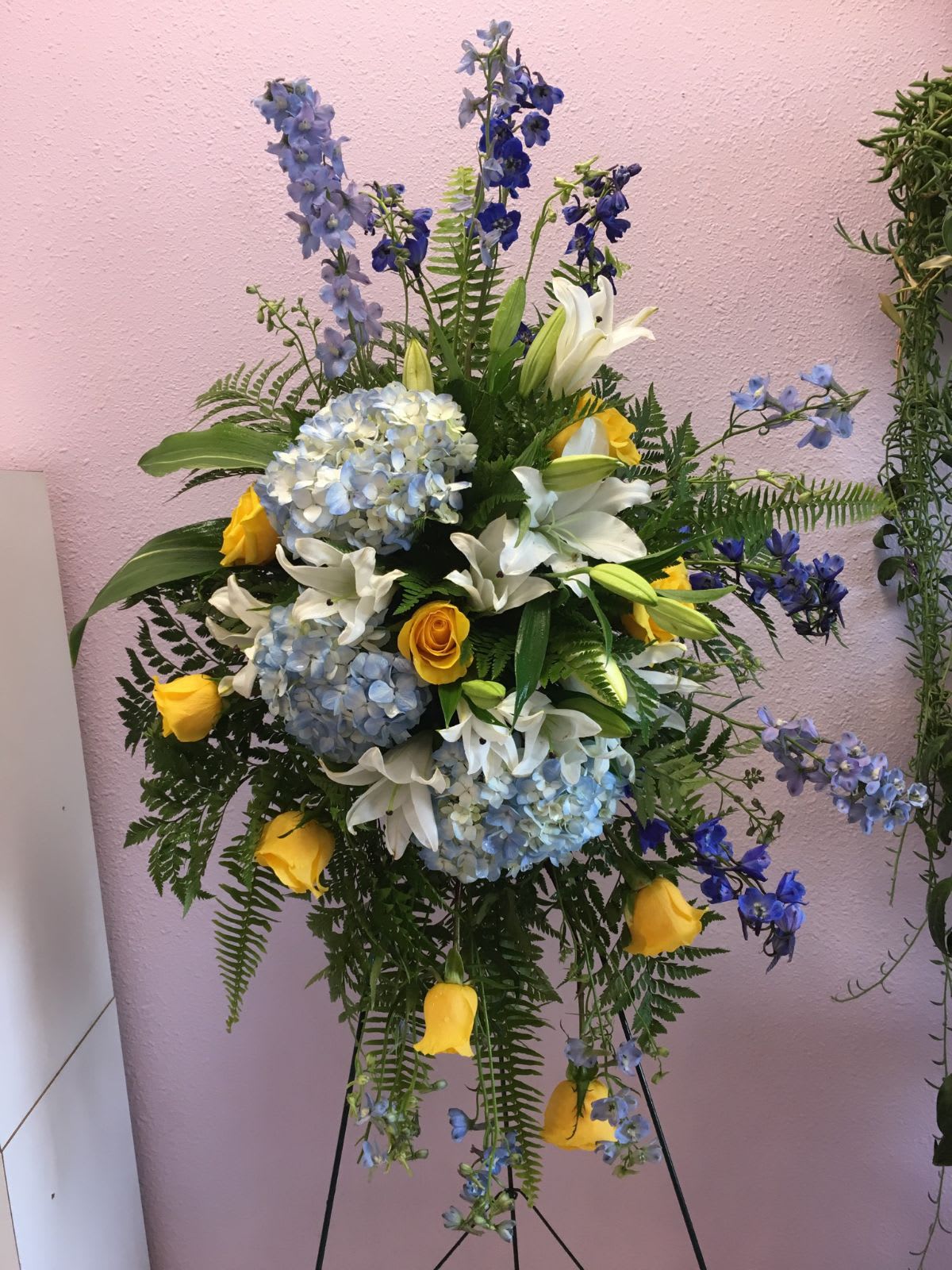 Standing floral spray with blue hydrangeas, white lilies, and yellow roses