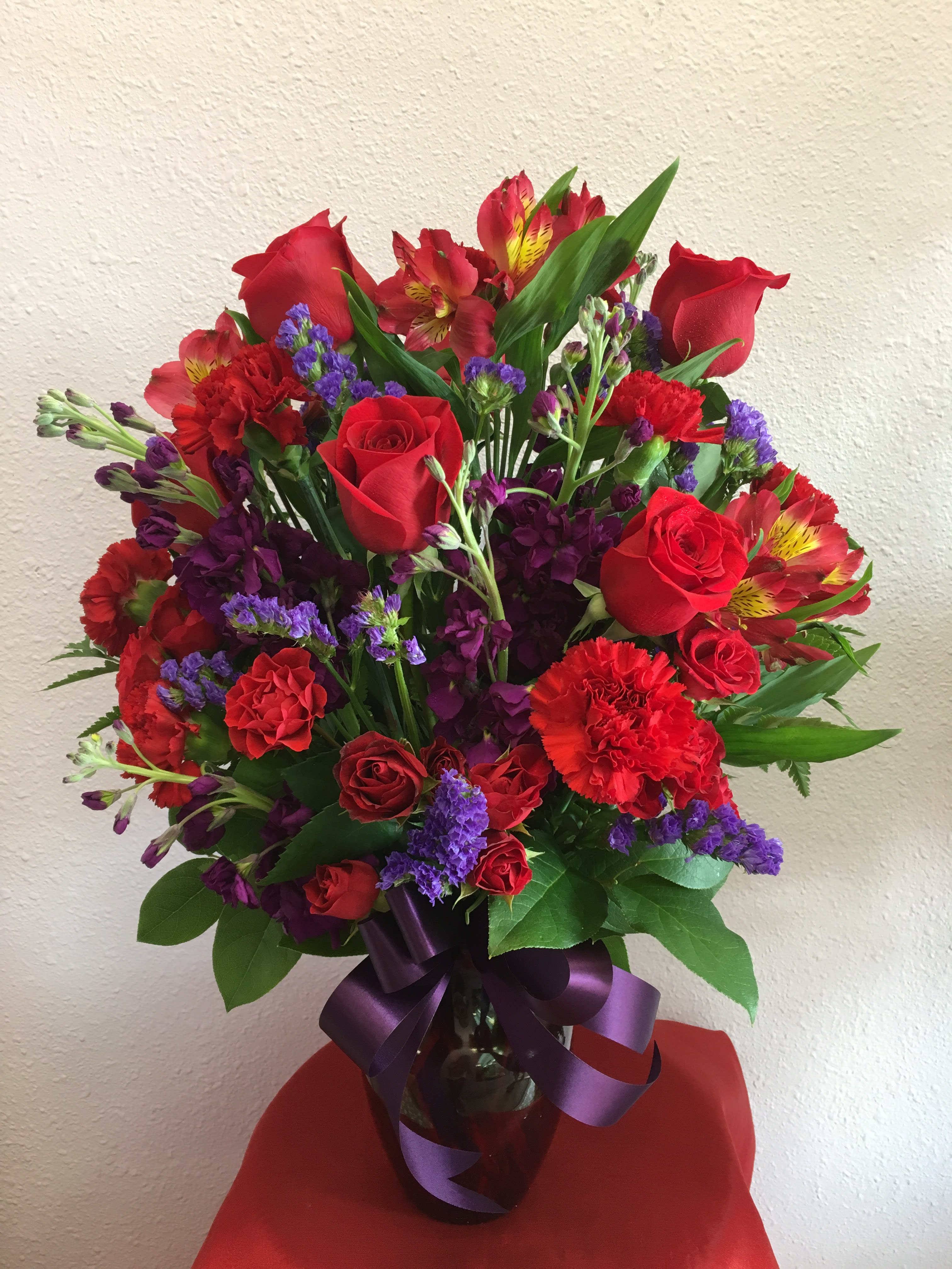 Bouquet of red roses, carnations, and purple filler in a glass vase