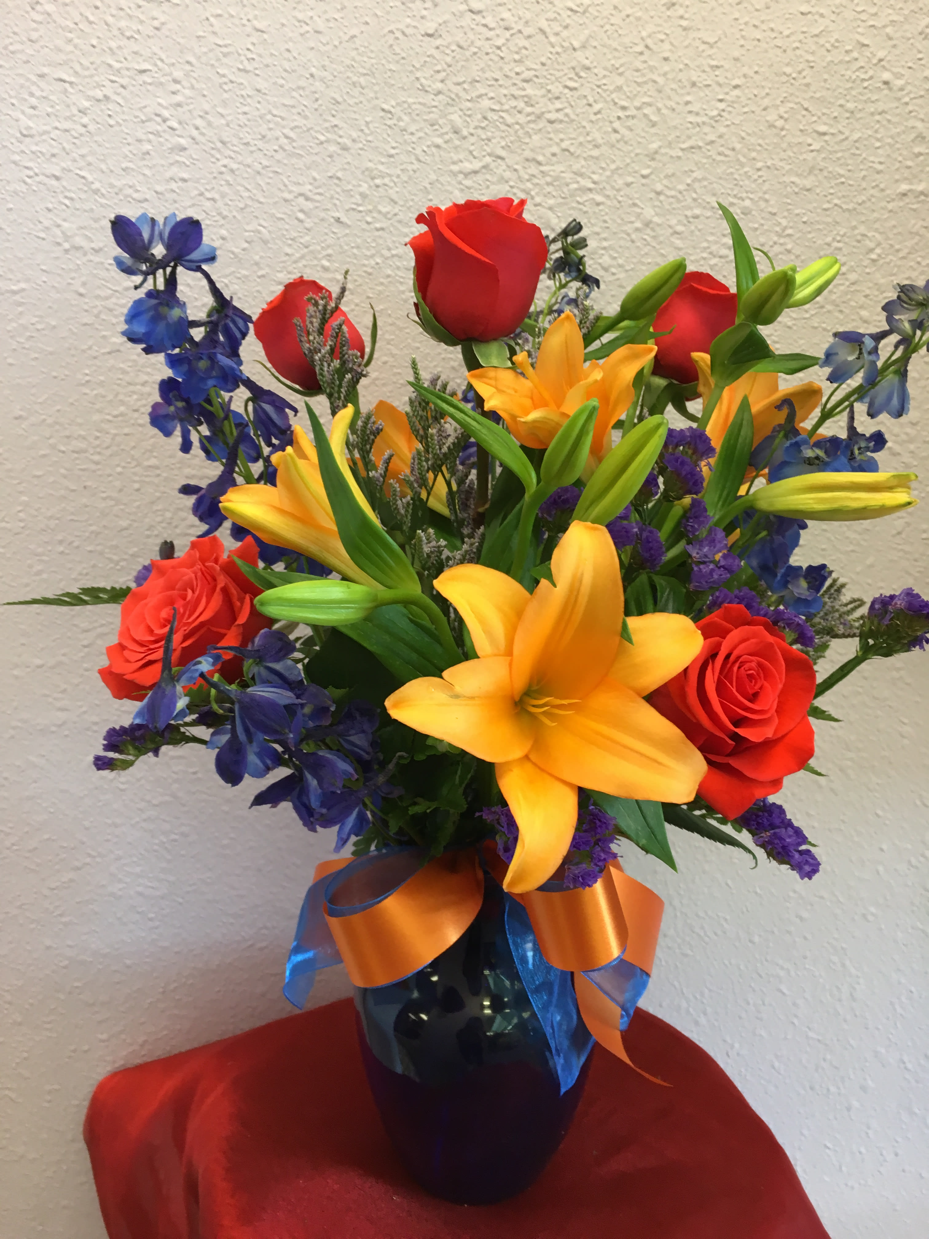Bouquet of red roses, yellow lilies, and blue flowers in a vase
