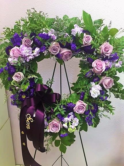 Purple and pink floral wreath on a stand with a ribbon bow