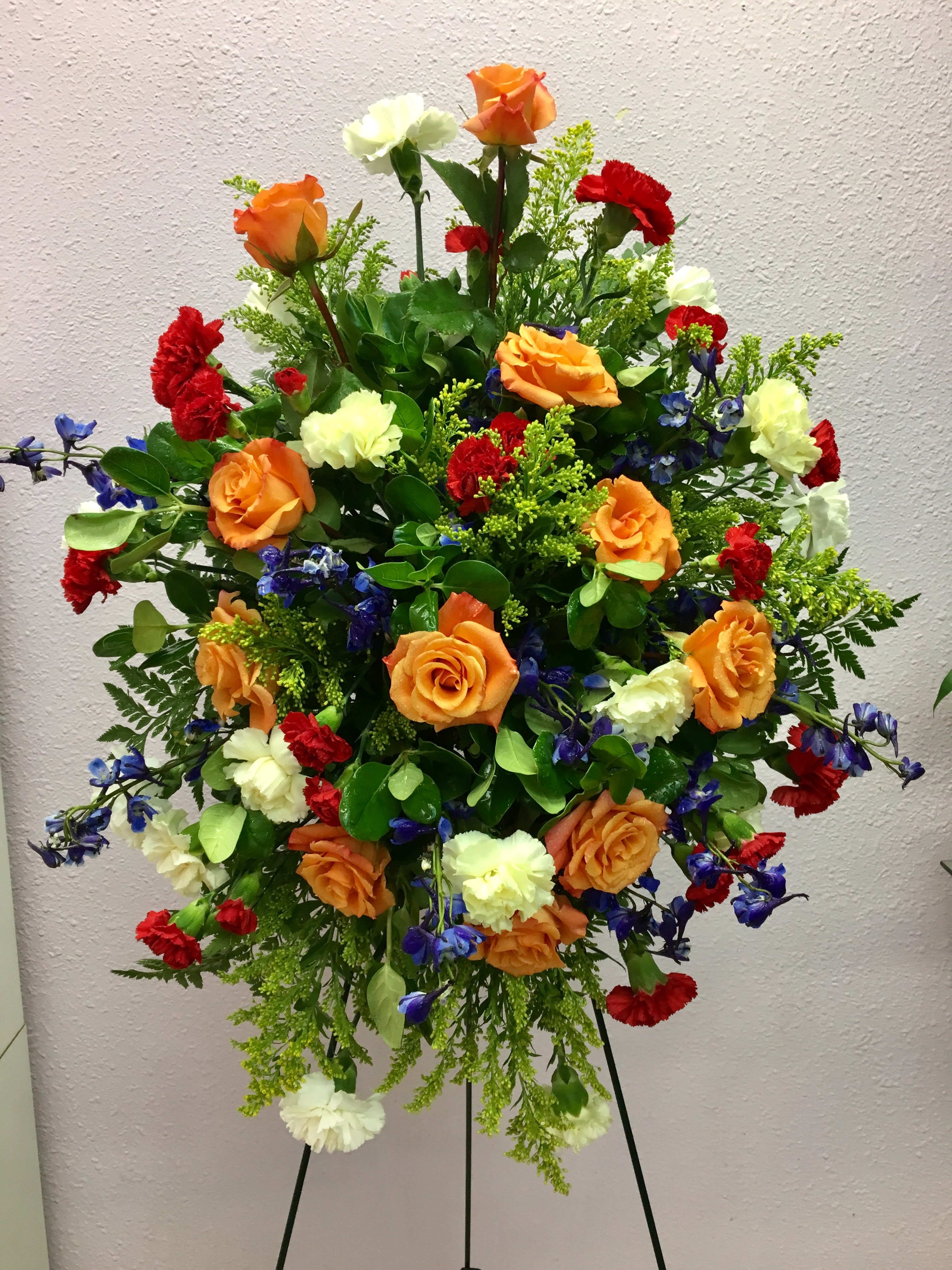 Large standing floral spray with orange roses, red carnations, and white blooms