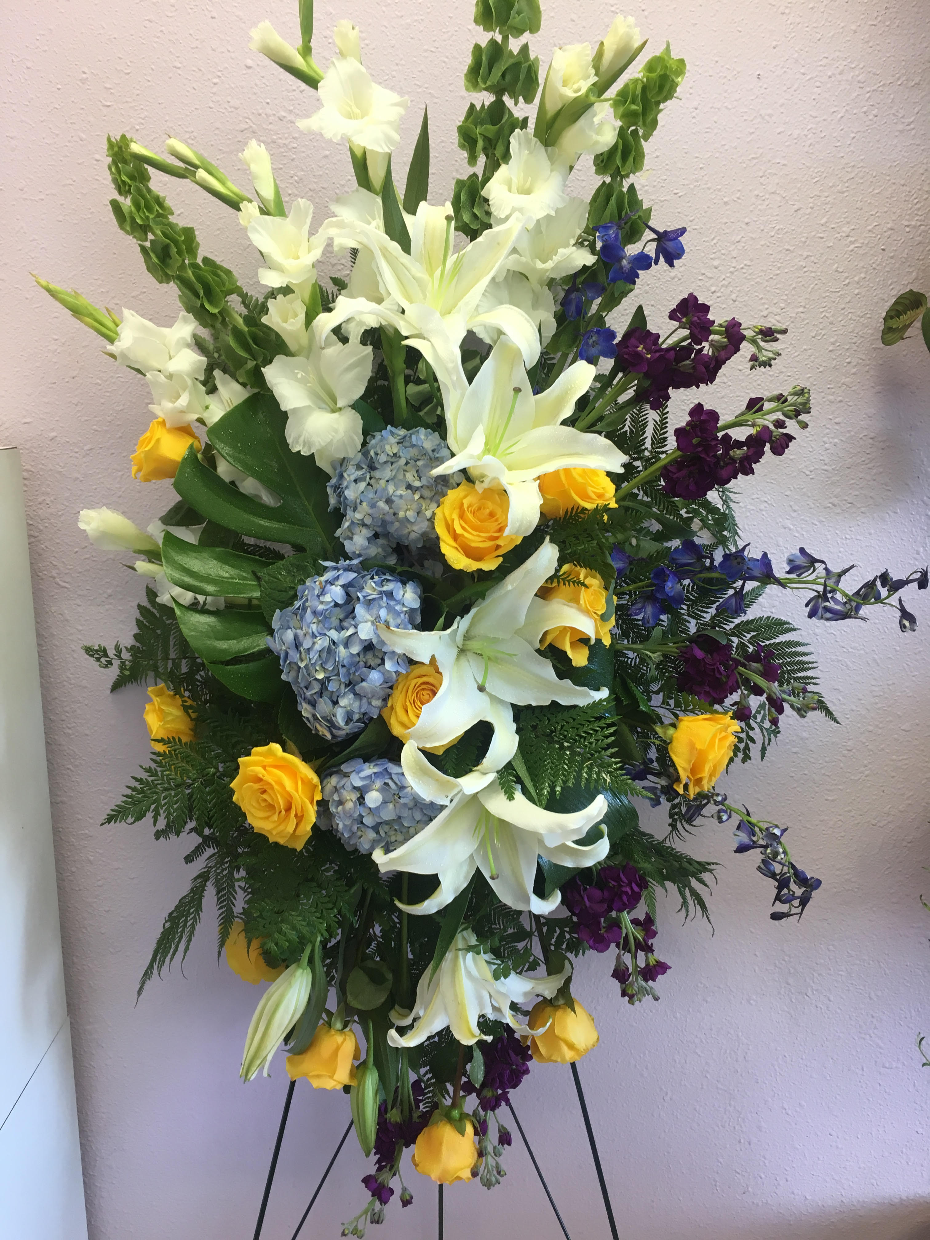 Tall floral spray with white lilies, yellow roses, blue hydrangeas, and purple accents