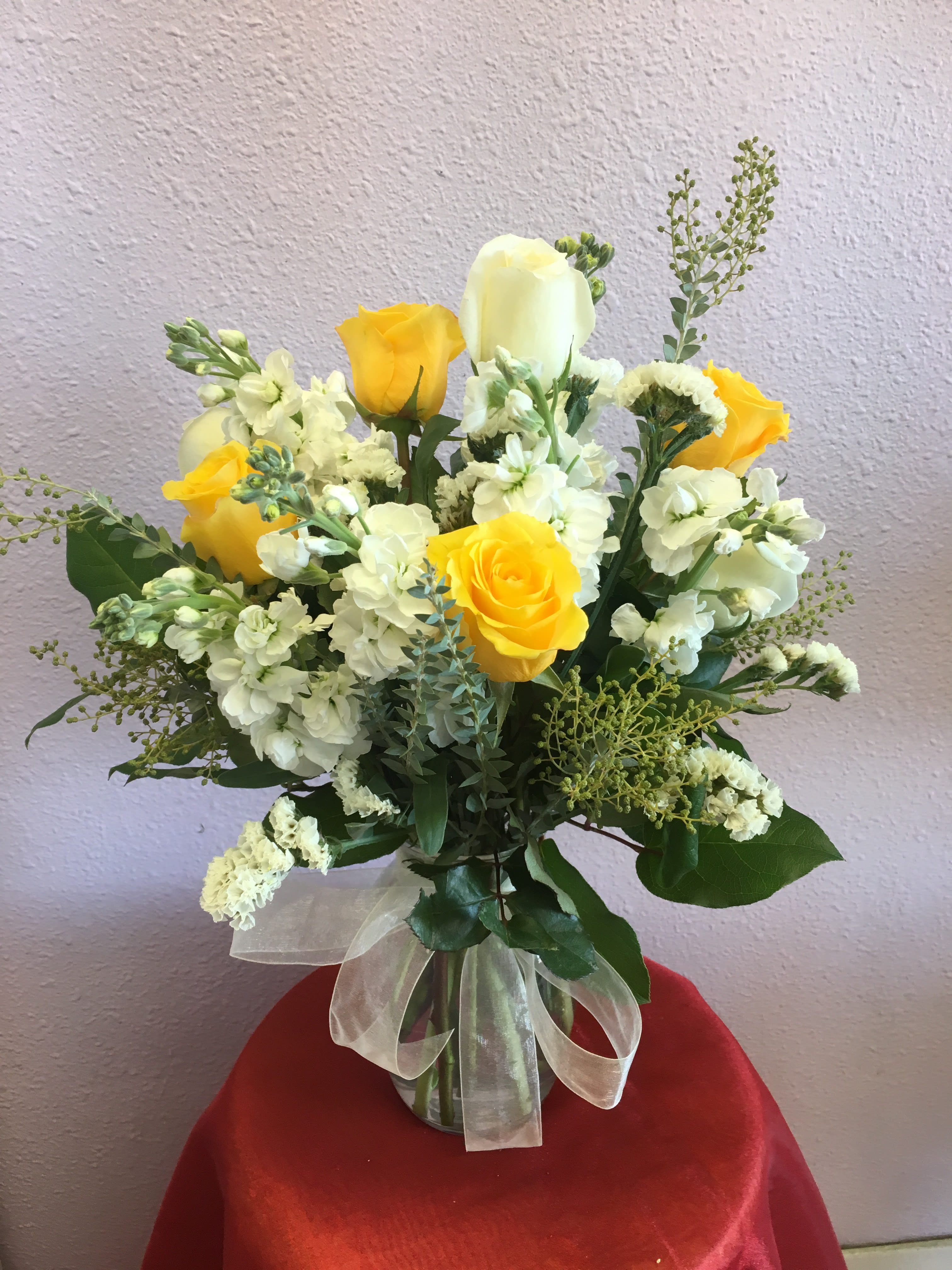 Yellow and white rose bouquet in a glass vase with a ribbon