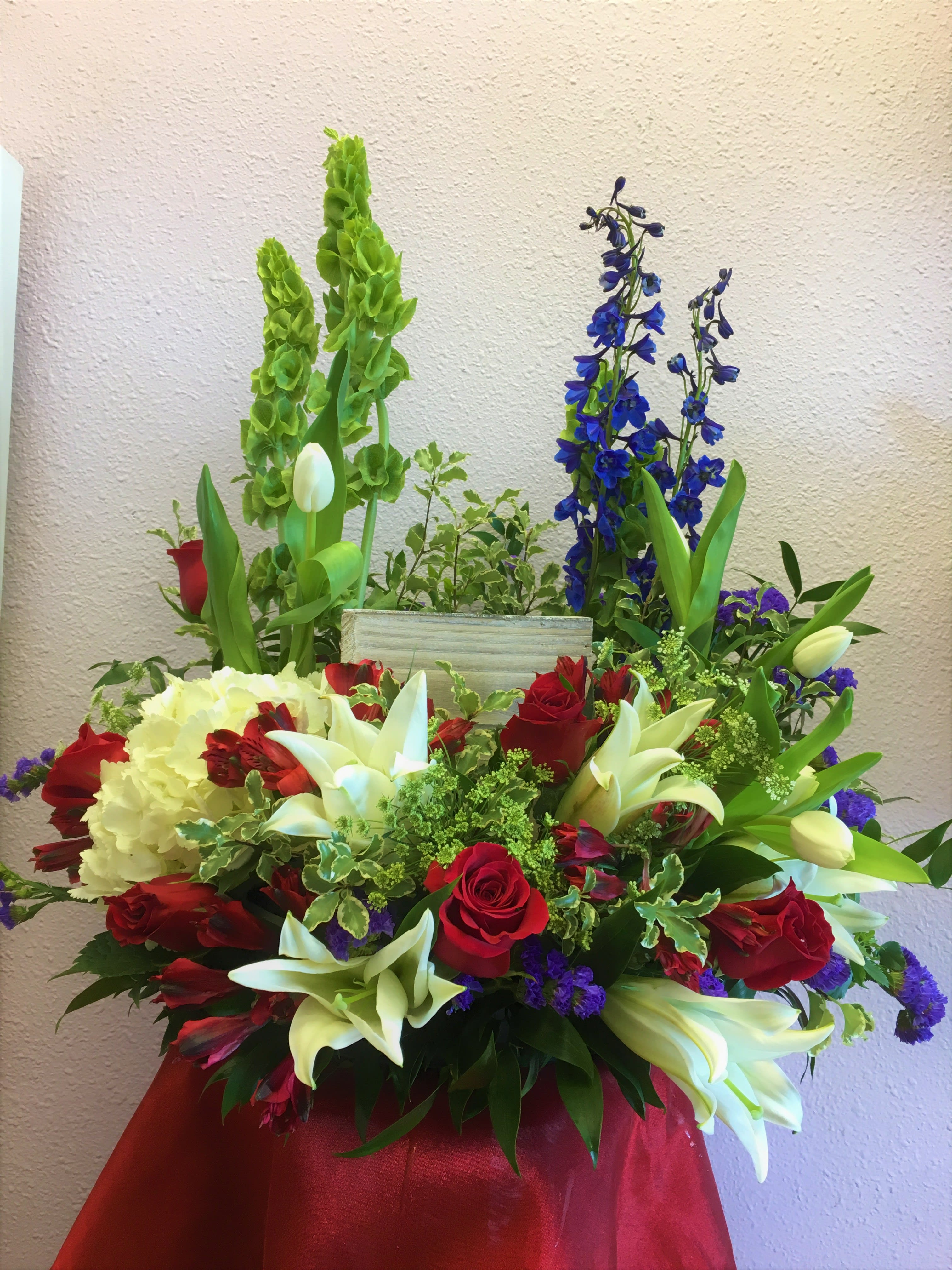 Large mixed floral arrangement with red roses, white lilies, and blue delphinium
