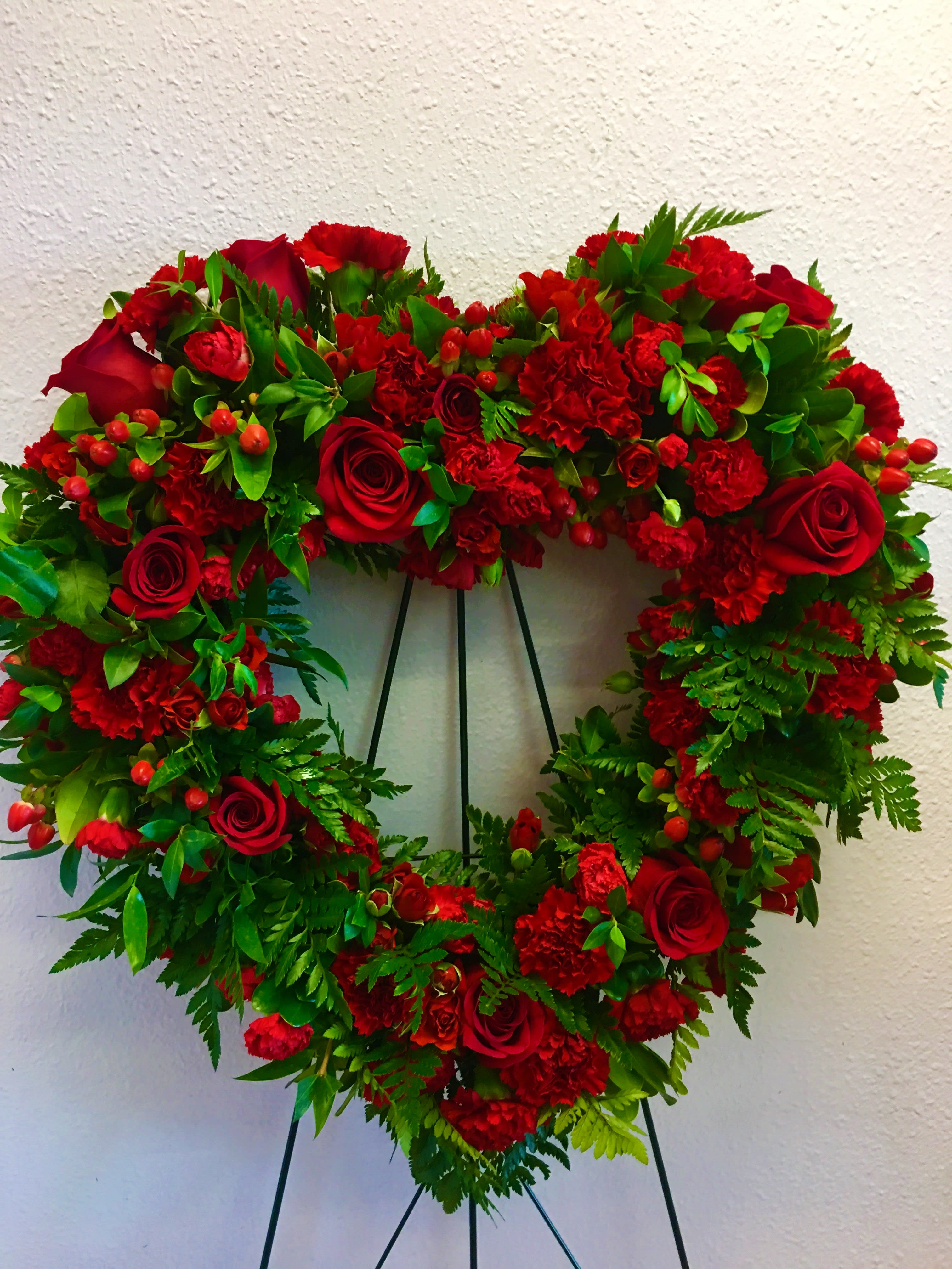 Heart-shaped wreath of red roses and carnations on a stand