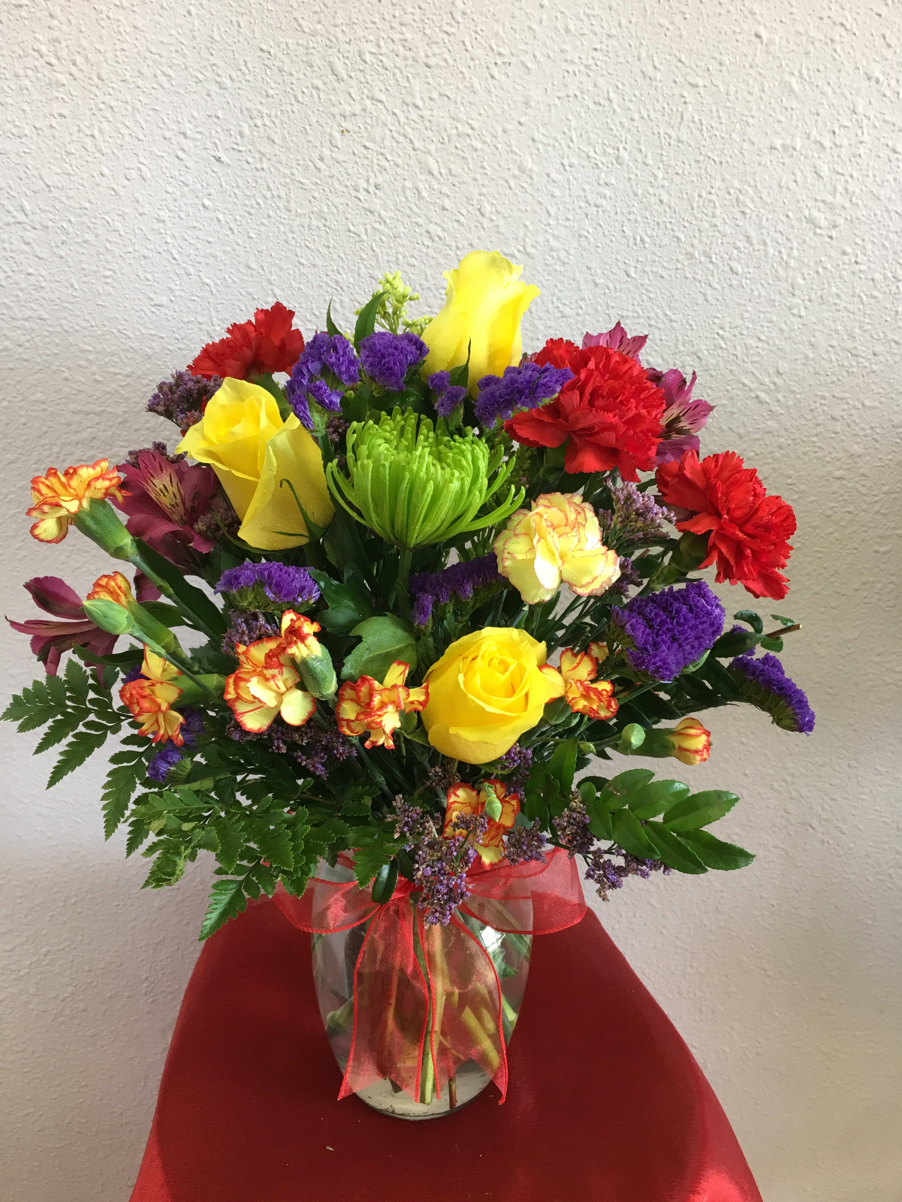 Colorful mixed bouquet with roses, carnations, and purple filler in a glass vase