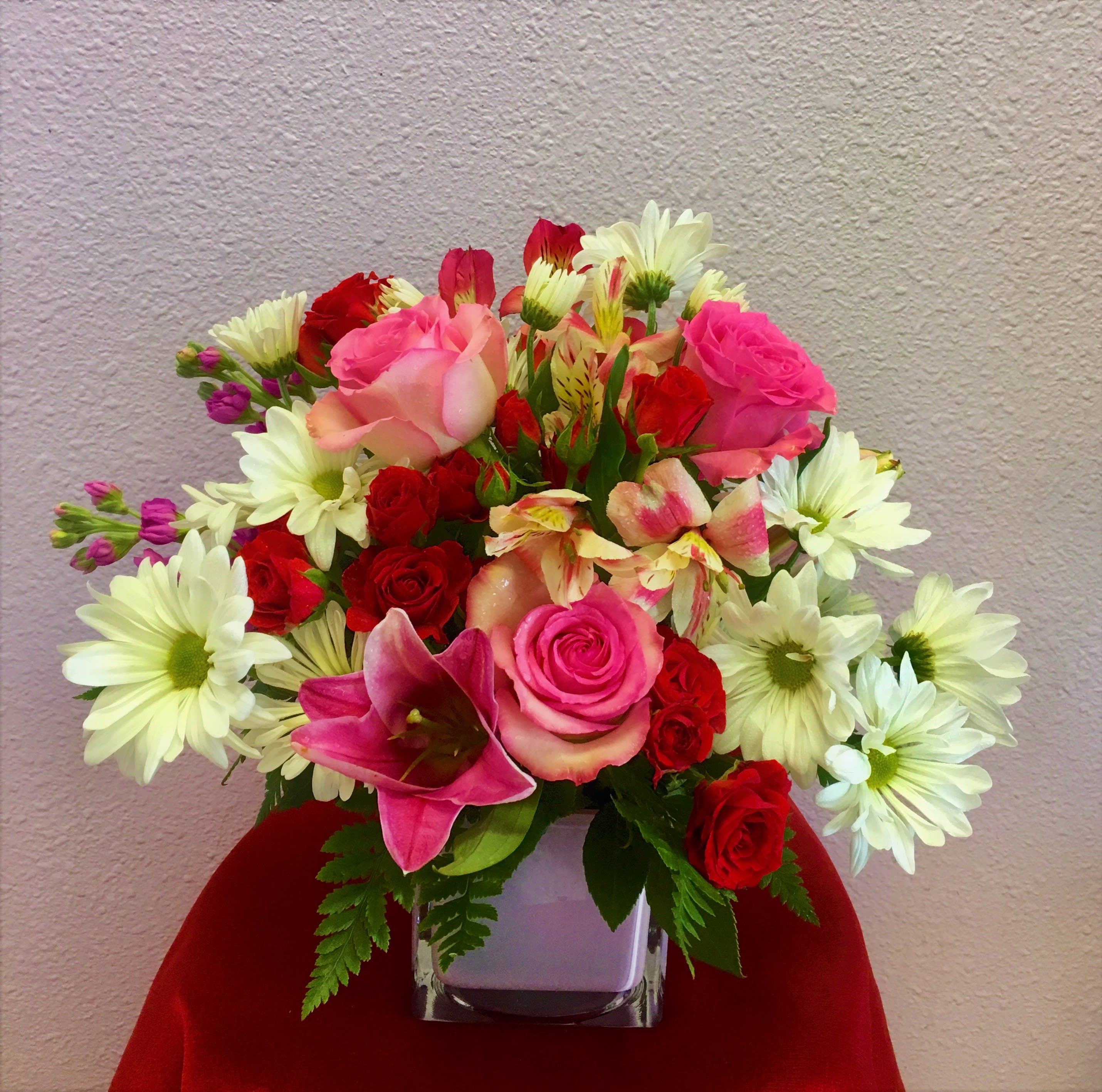 Mixed bouquet of pink and red roses with white daisies in a square vase