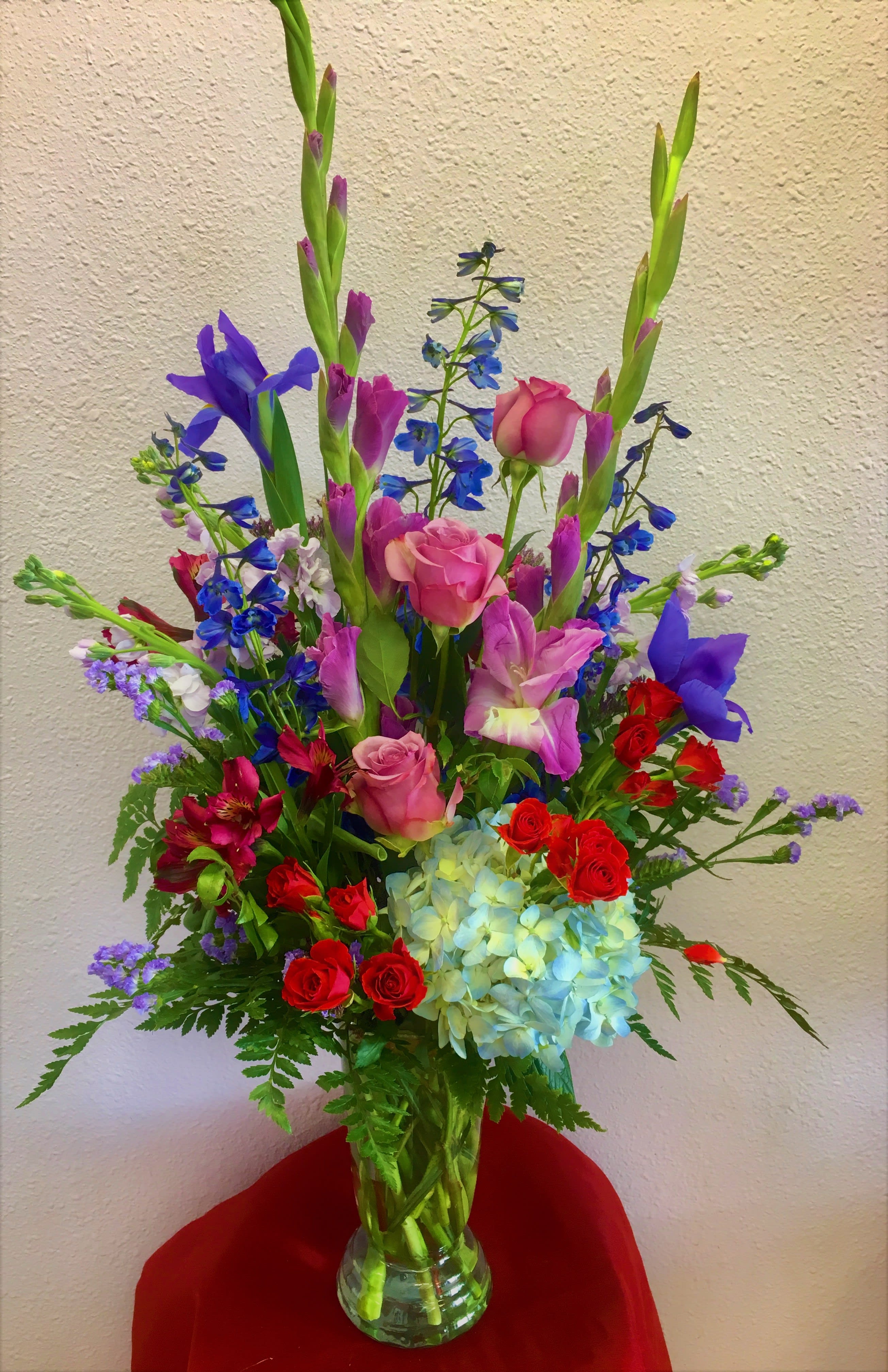 Tall mixed bouquet in a clear glass vase with pink roses and blue flowers