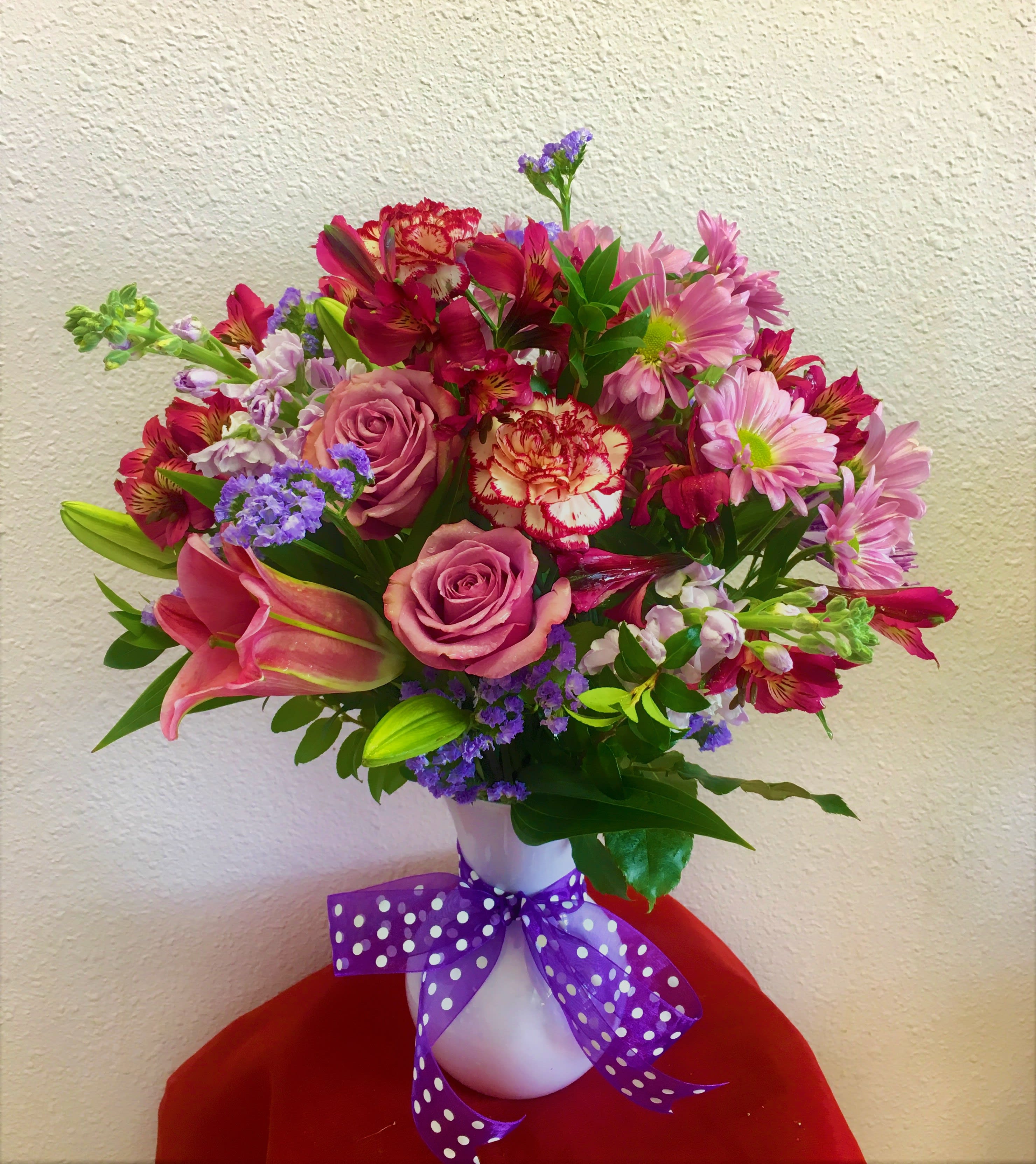 Mixed bouquet of pink and purple flowers in a white vase with a purple ribbon