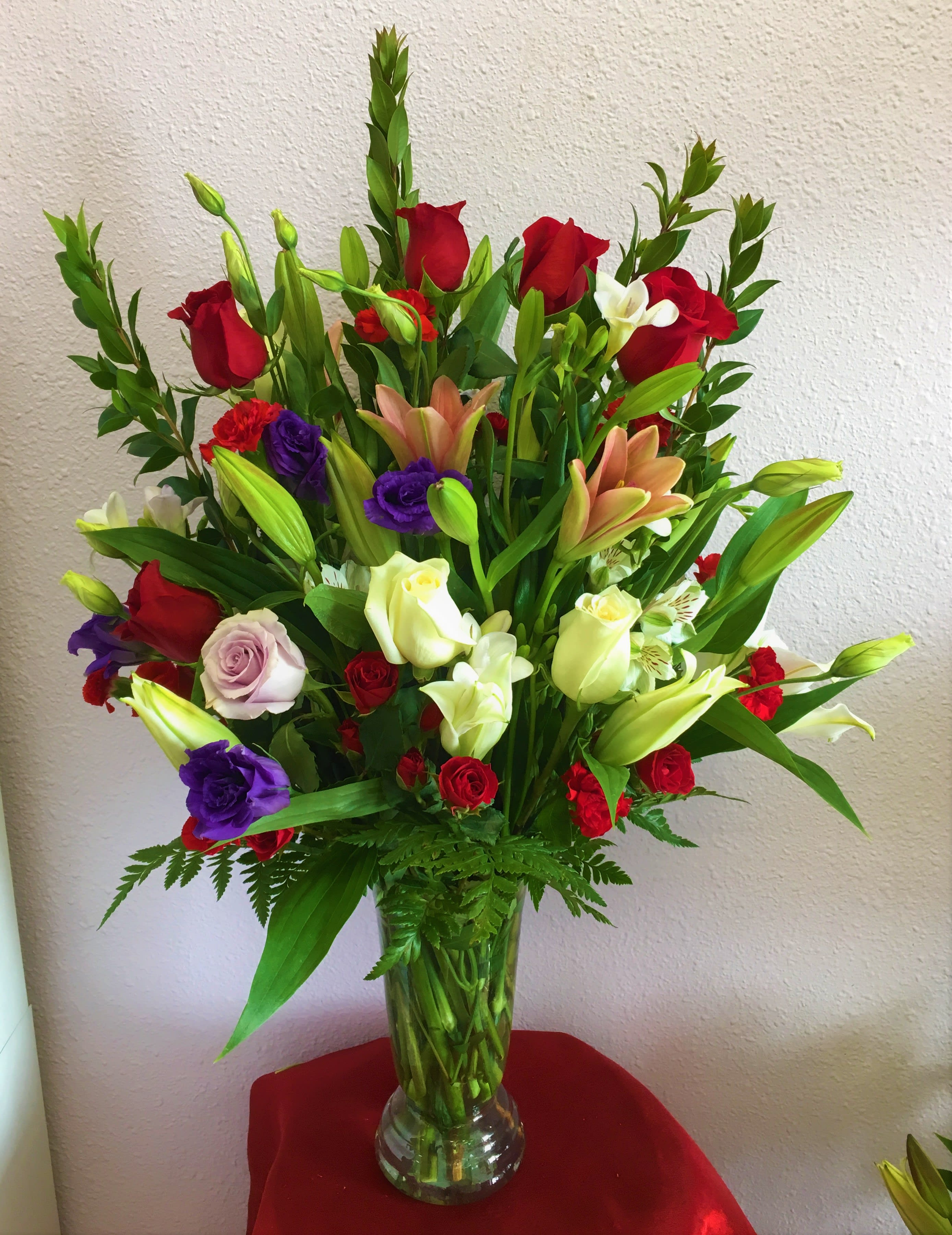 Tall mixed bouquet of roses, lilies, and orchids in a clear glass vase