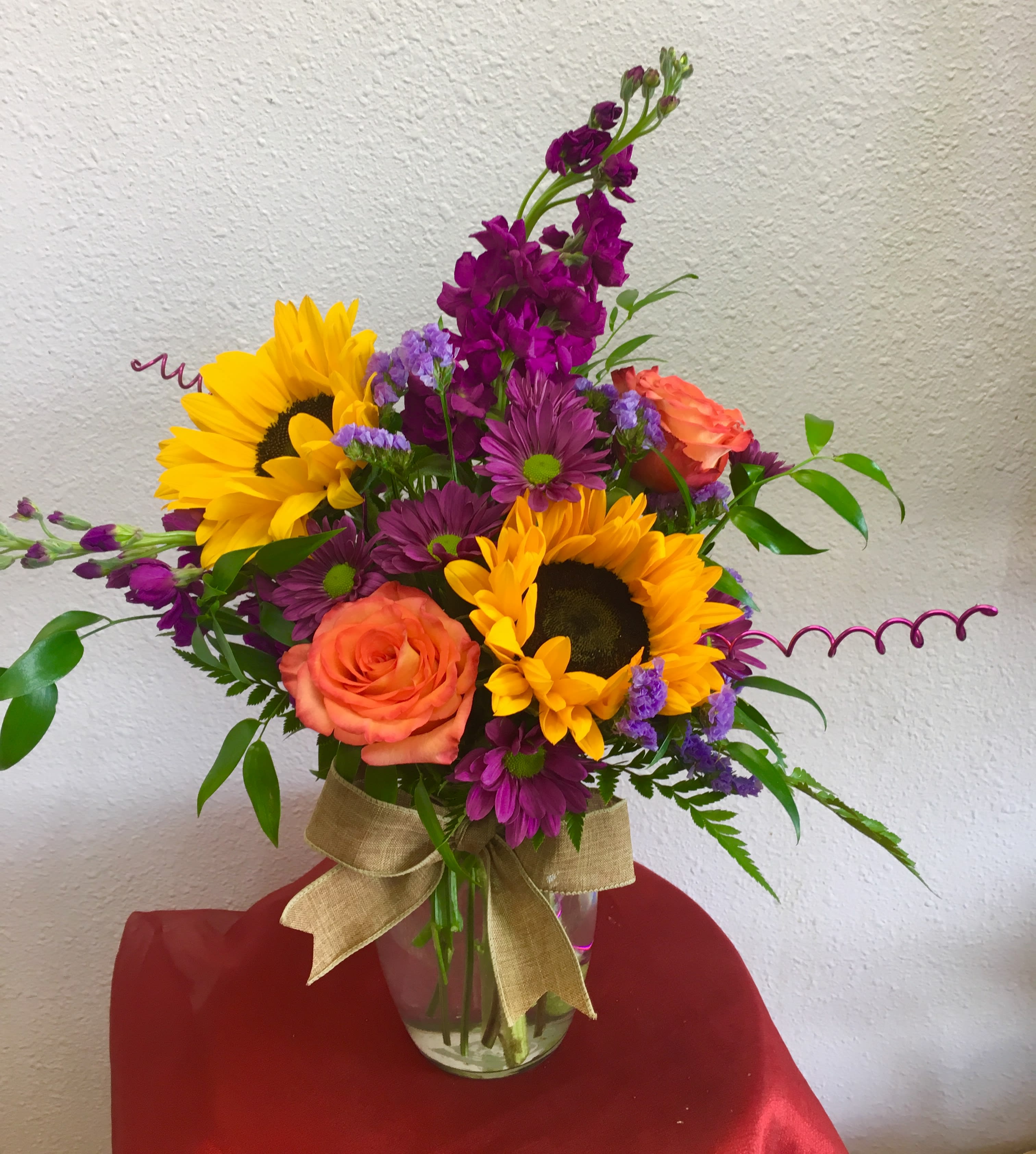 Bouquet of sunflowers, purple blooms, and orange roses in a glass vase