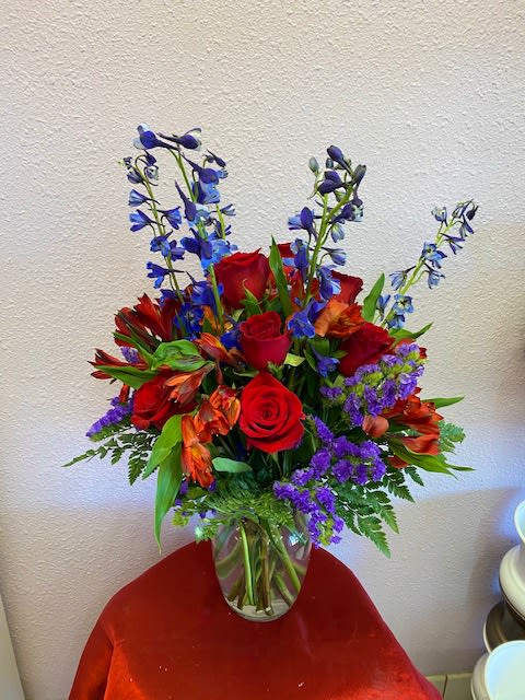 Bouquet of red roses, orange flowers, and blue delphinium in a glass vase