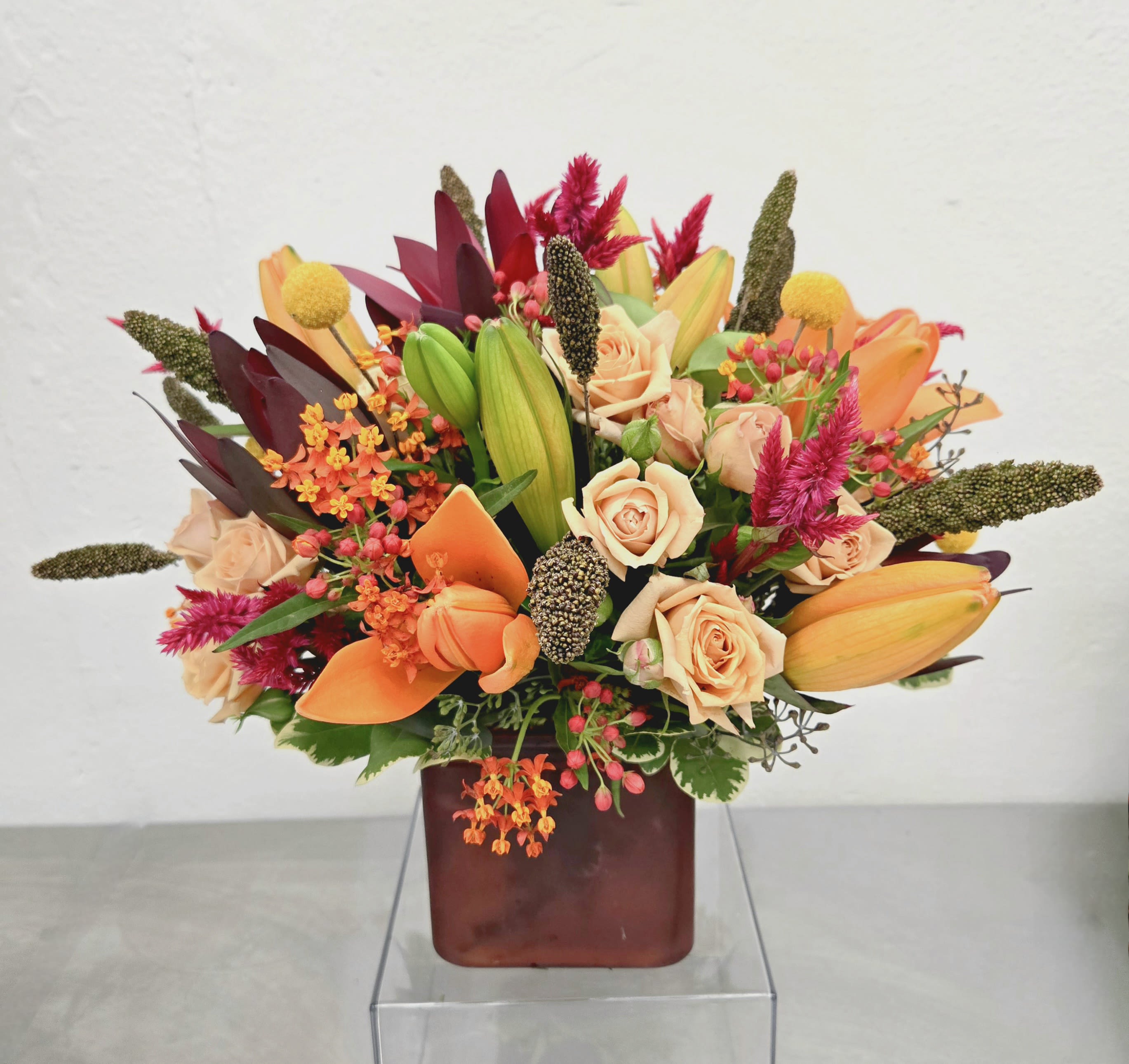 Mixed bouquet of peach roses, orange lilies, and pink accents in a square vase