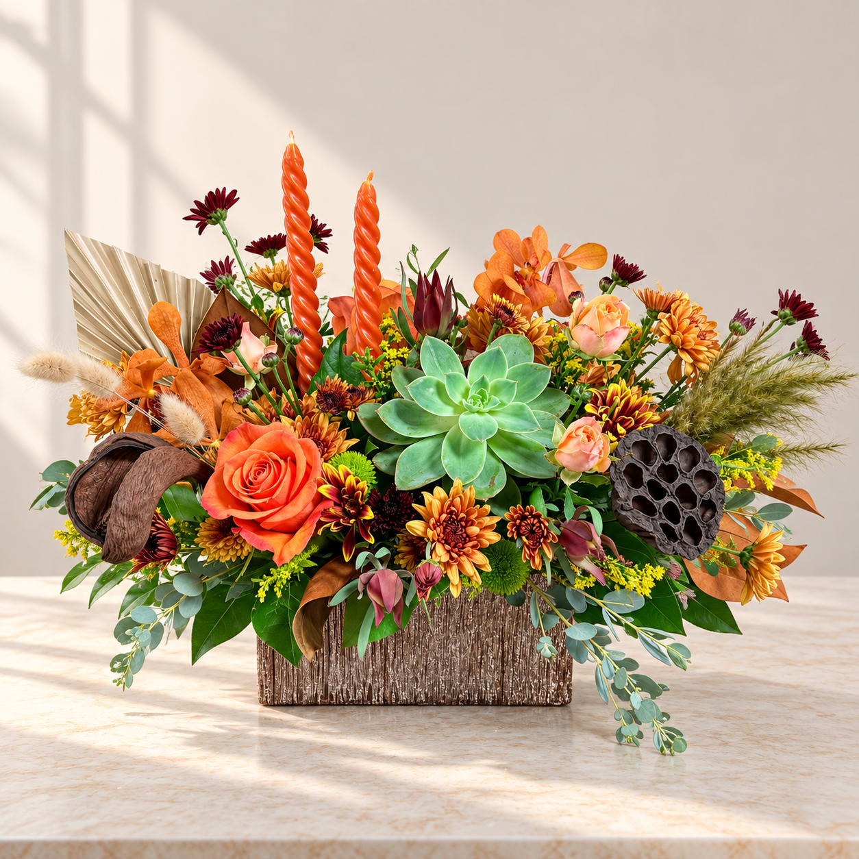 Autumn floral arrangement with succulents, roses, and orange candles in a textured container