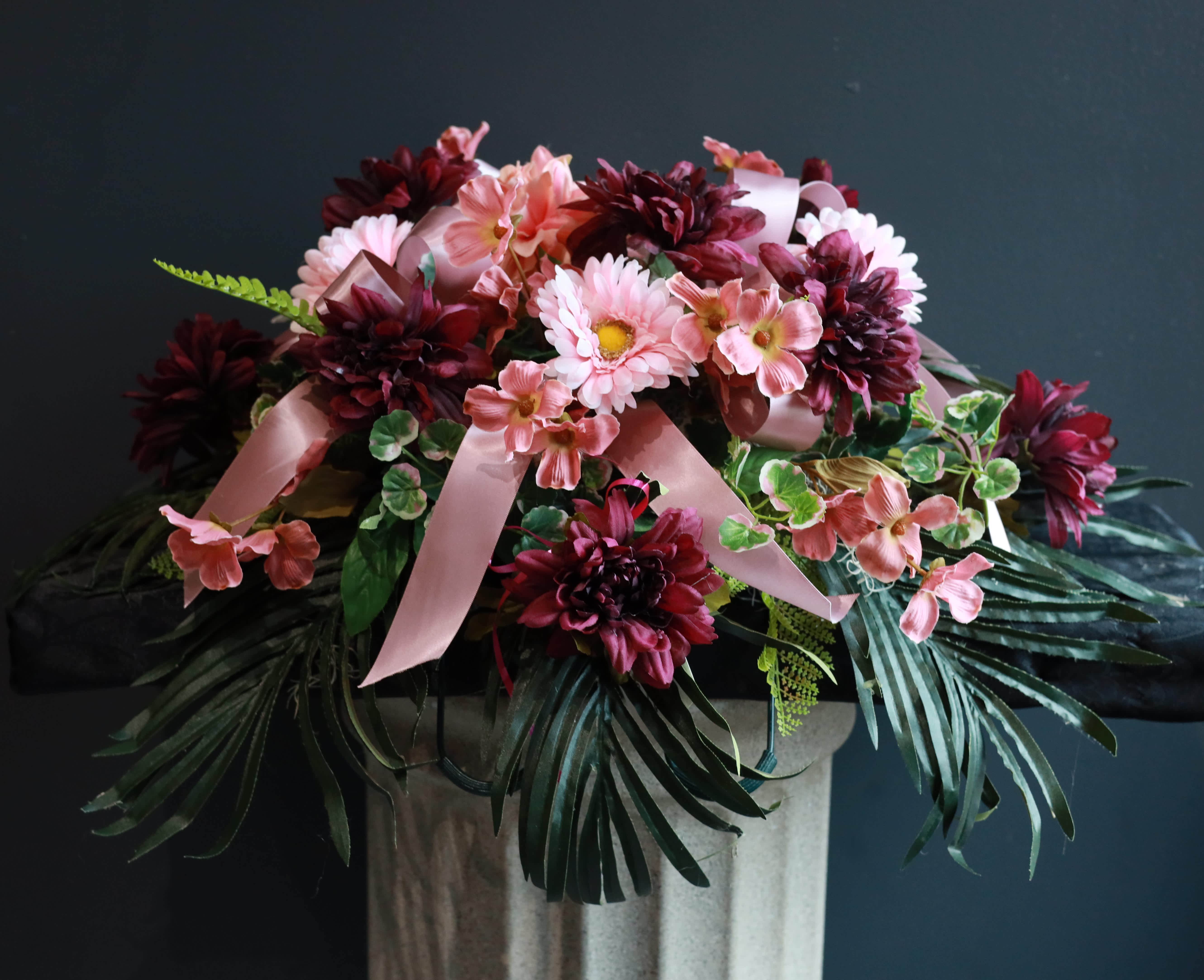 Pink and burgundy floral arrangement with ribbon on a pedestal