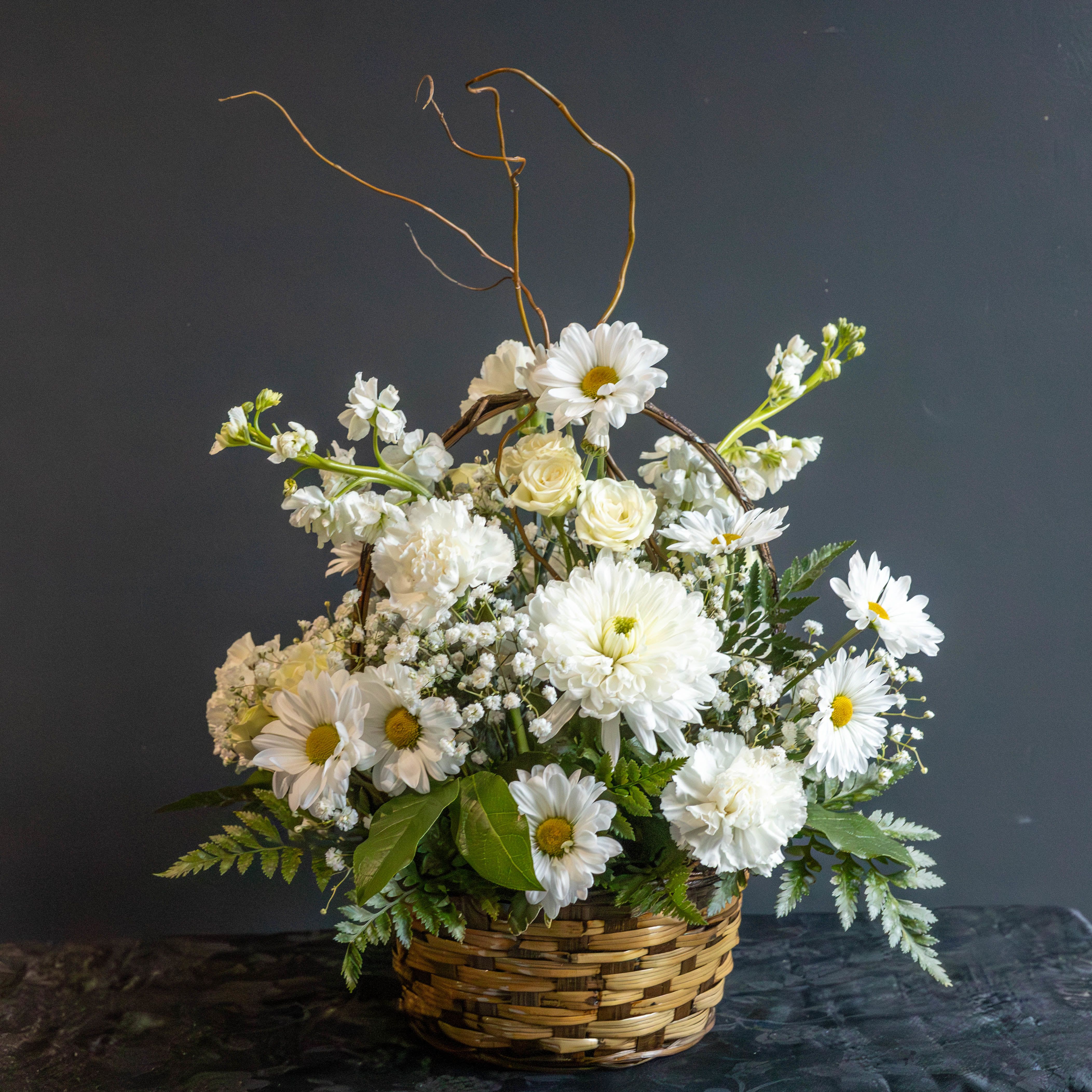 White flowers arranged in a wicker basket with tall curly branches