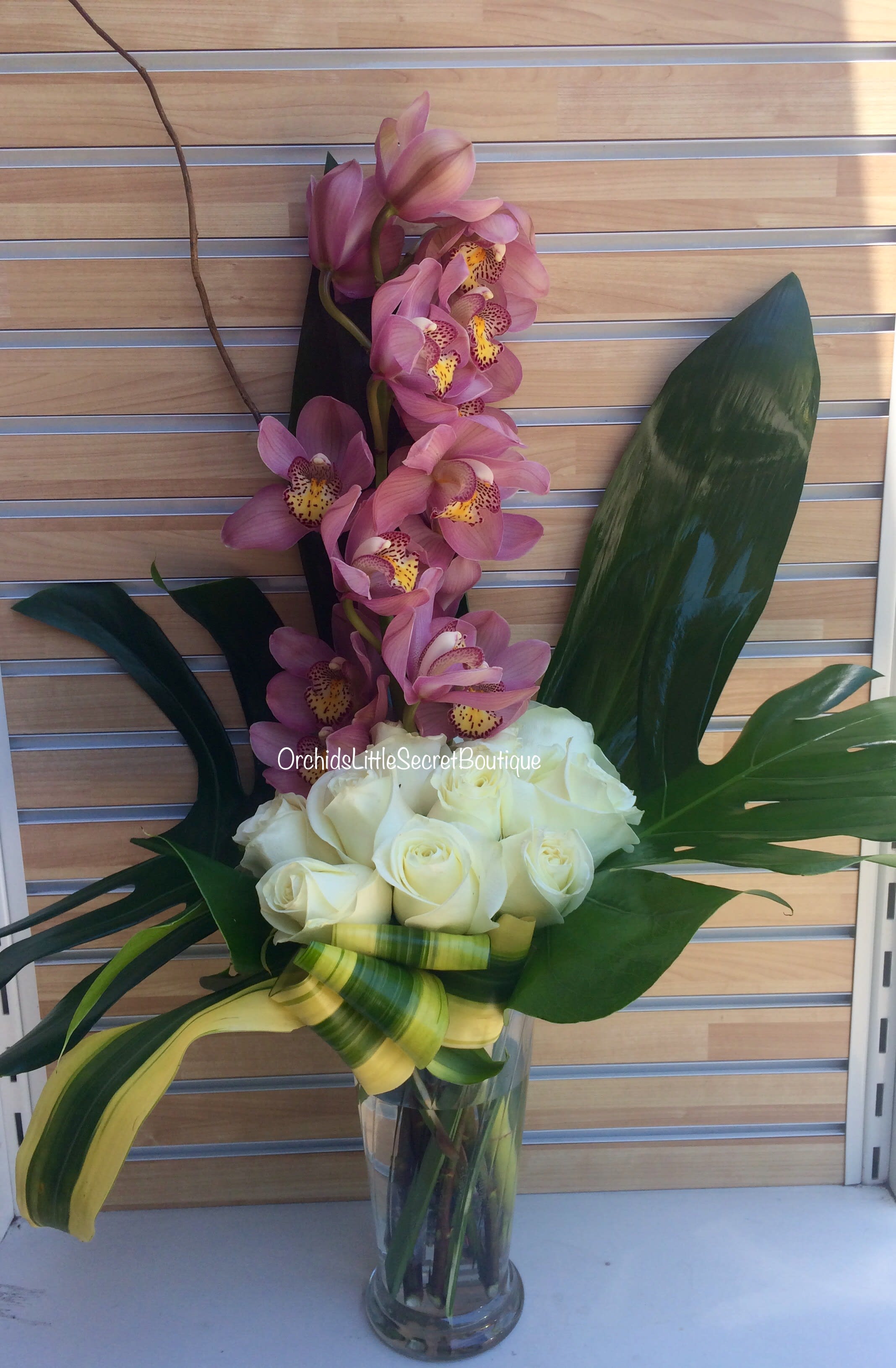 Pink orchids and white roses in a clear glass vase with large tropical leaves
