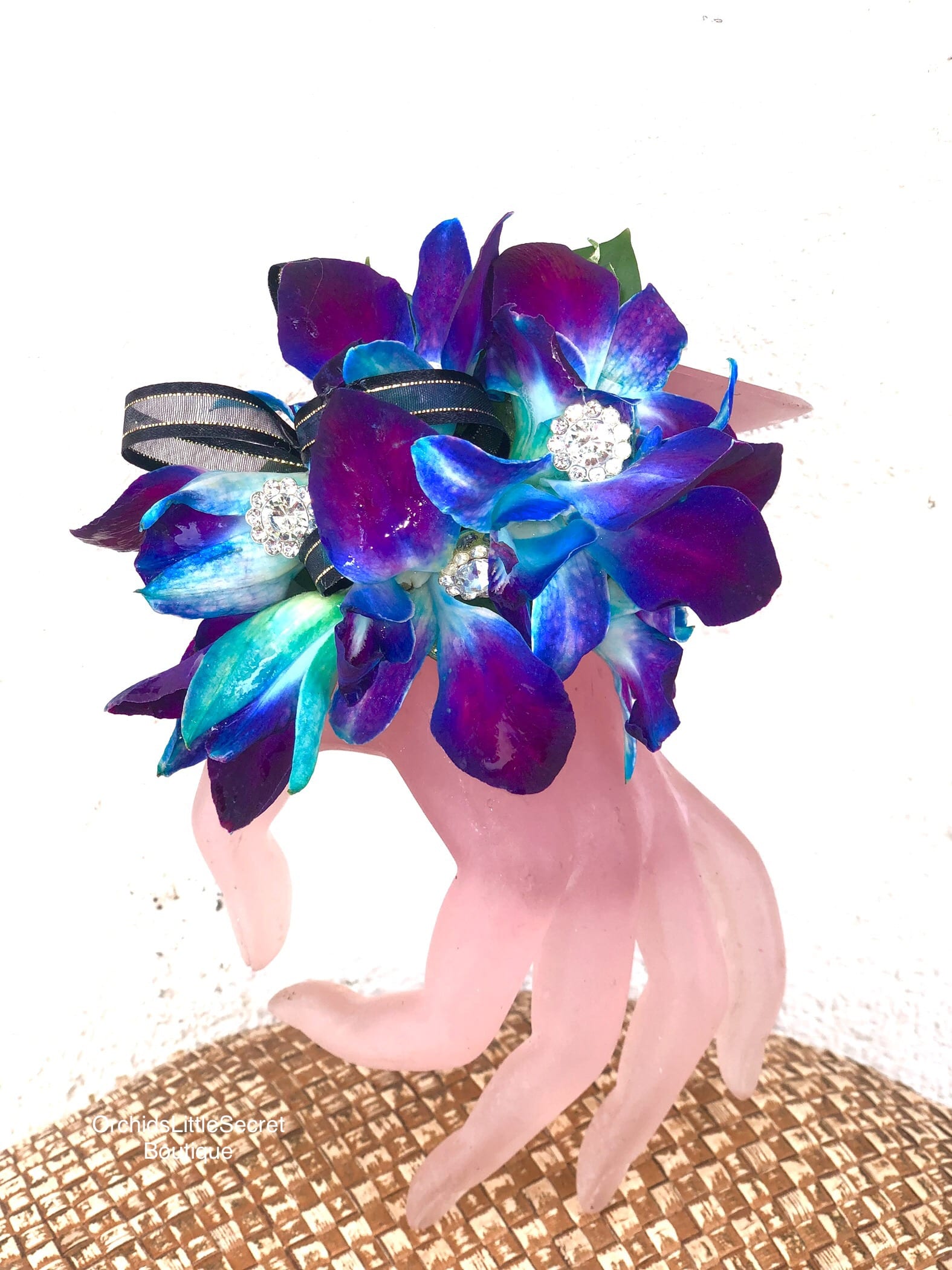 Blue and purple orchid boutonniere on a pink hand-shaped stand