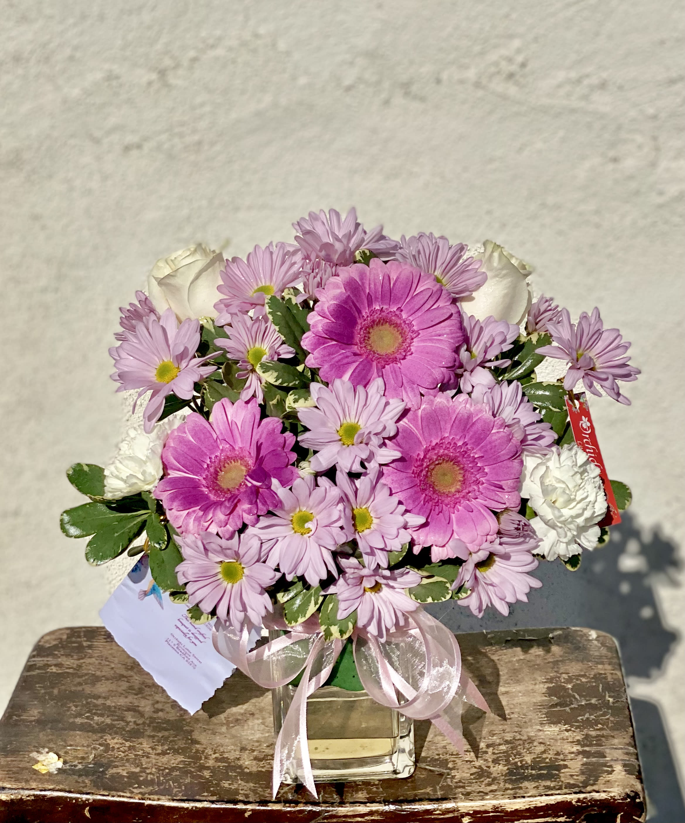 Pink gerberas and daisies arranged in a clear glass vase with a ribbon.