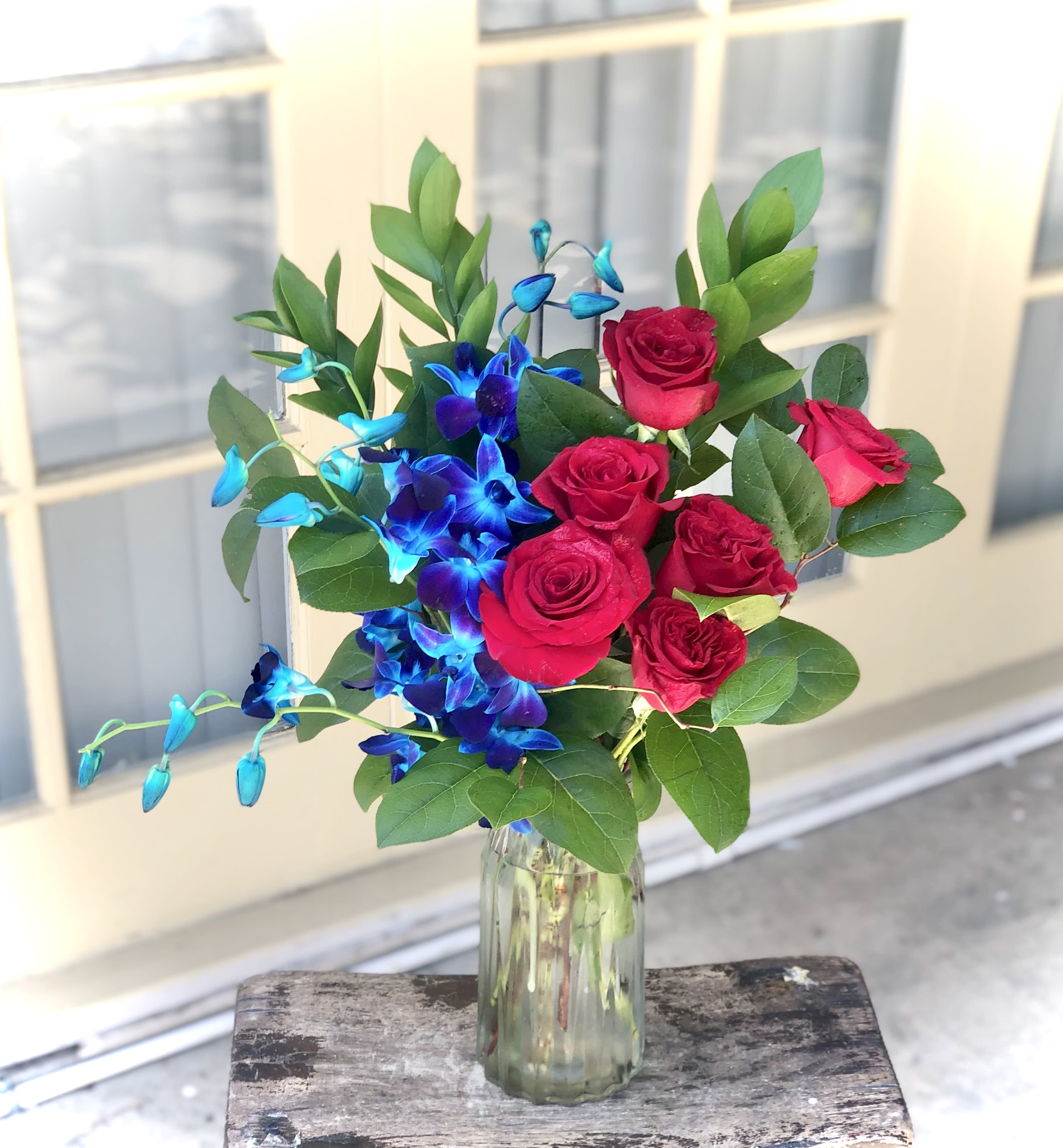 Bouquet of red roses and blue orchids in a glass vase