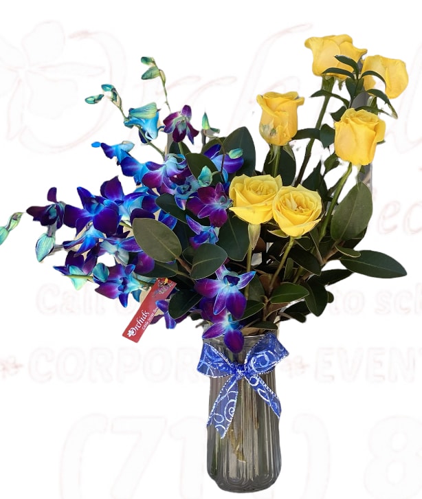 Yellow roses and blue orchids in a glass vase with a blue ribbon.