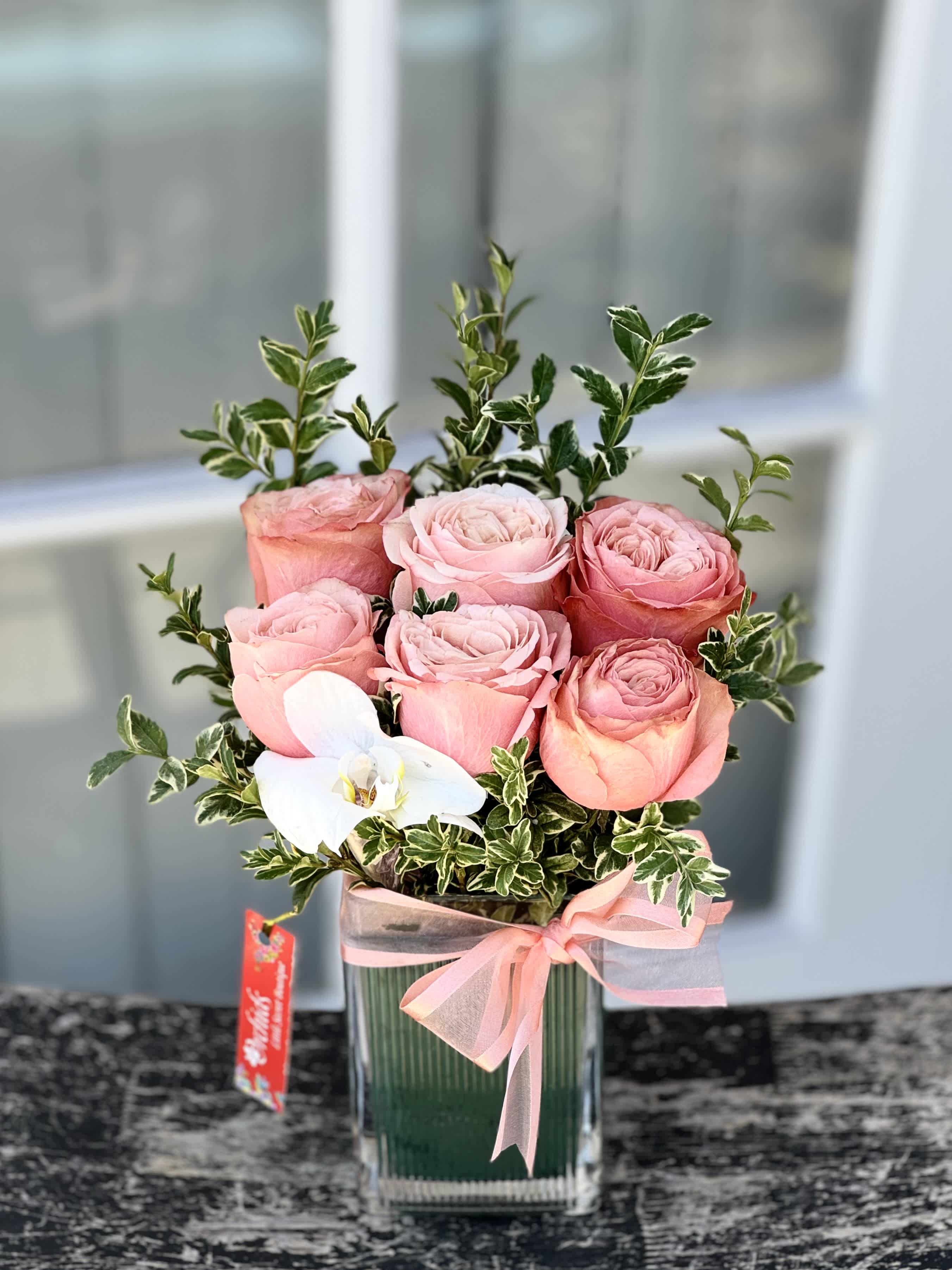 Pink roses in a glass vase with a white orchid and ribbon
