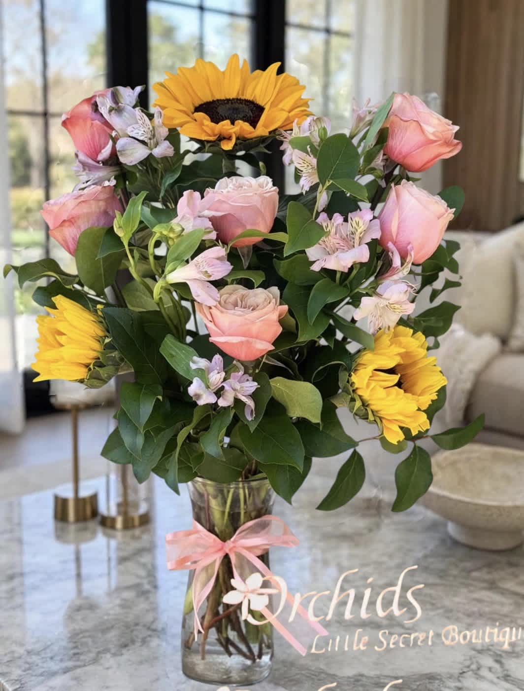 Pink roses and yellow sunflowers in a glass vase with a pink ribbon