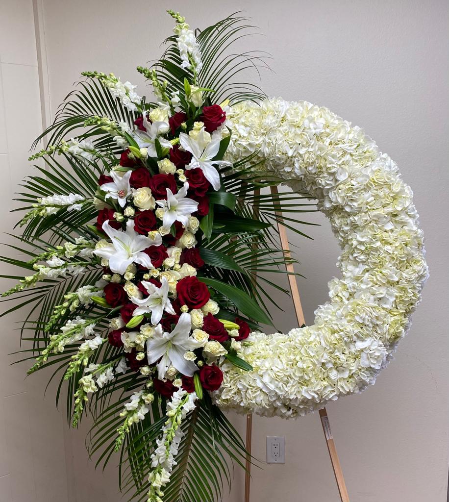 Large floral funeral wreath with red roses, white lilies, and white hydrangeas