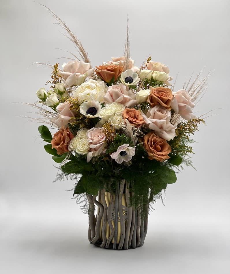 Bouquet of blush and peach roses with white accent flowers in a tall vase