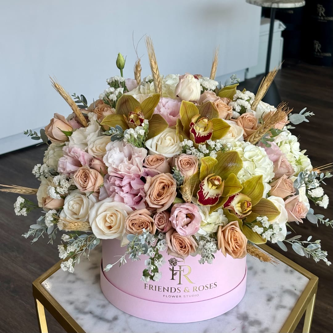 Large pastel flower arrangement in a pink round box with roses and orchids