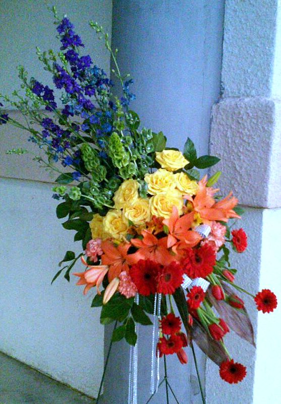 Beyond The Rainbow - Beyond the Rainbow by Windmill Floral Expressions, Las Vegas  A vivid celebration of love, memory, and eternal light, Beyond the Rainbow is a radiant standing spray designed to honor a life lived with joy and color. This bold arrangement features a symphony of hues—sunny yellow roses, fiery orange lilies, rich red gerberas, and vibrant purple larkspur—all flowing together like the colors of a brilliant rainbow after the storm.  Crafted with care by Windmill Floral Expressions in Las Vegas, Beyond the Rainbow offers a message of hope, peace, and the beauty that lies just beyond what we can see. It’s a perfect tribute for someone whose spirit brought brightness to every life they touched, and whose legacy continues to shine.  