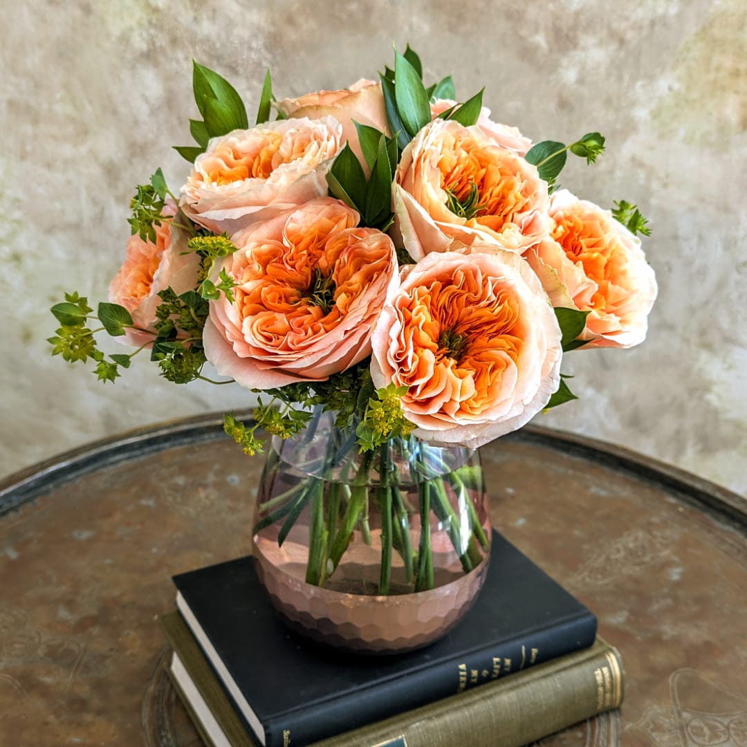 Peach roses arranged in a glass vase on stacked books