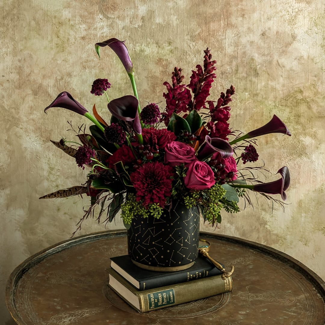 Dark burgundy floral arrangement in a black patterned vase on stacked books