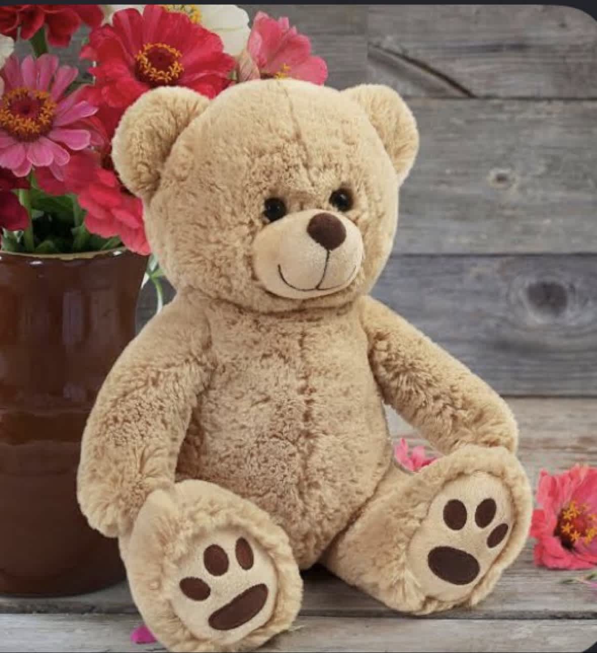 Teddy bear beside a vase of pink flowers