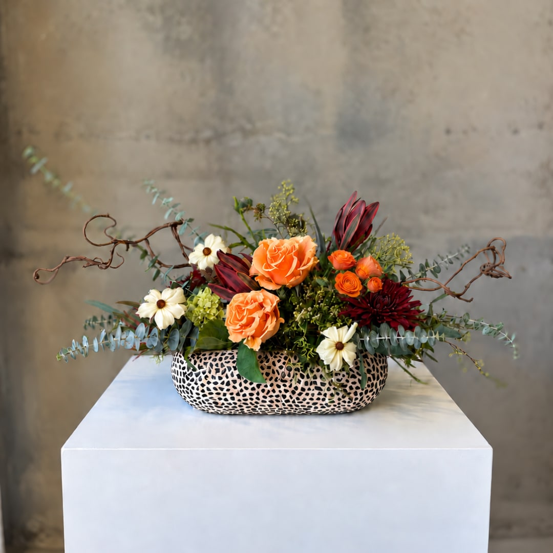 Orange and burgundy floral arrangement in a patterned low vase